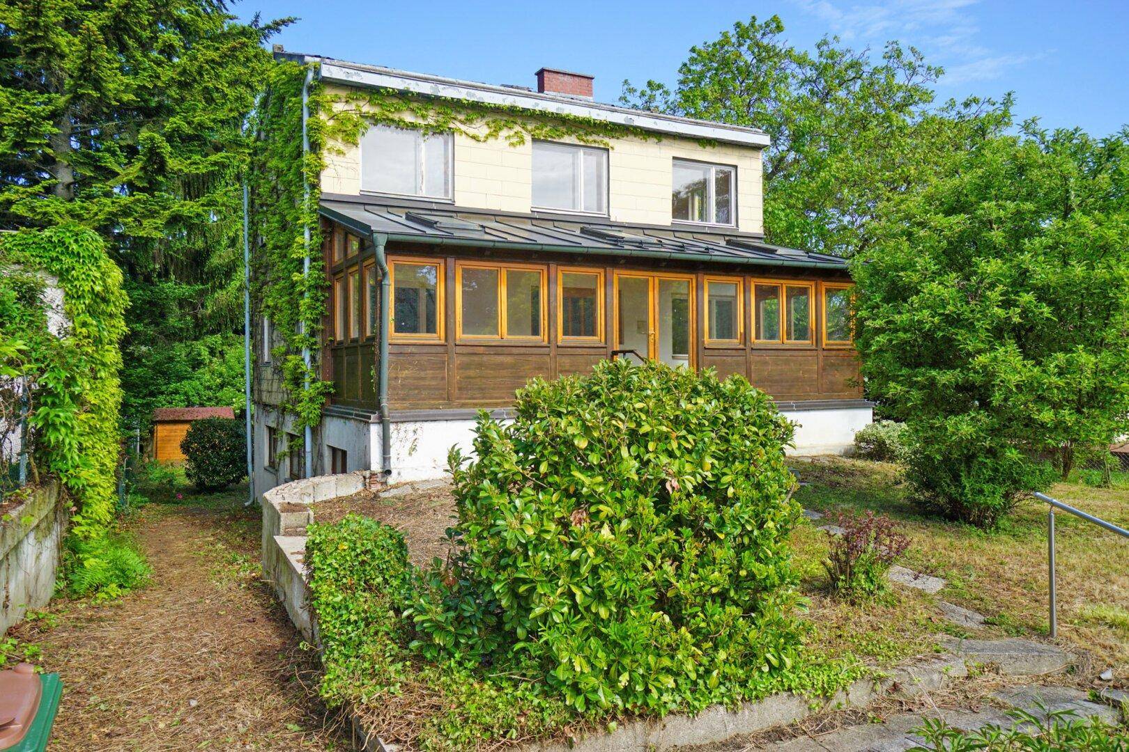 Seitenansicht des Hauses mit Wintergarten und üppigem Grün im Gartenbereich.