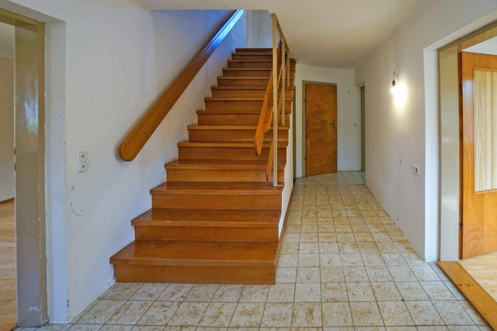 Heller Flur mit Holztreppe und Fliesenboden, der zu den oberen Etagen führt.
