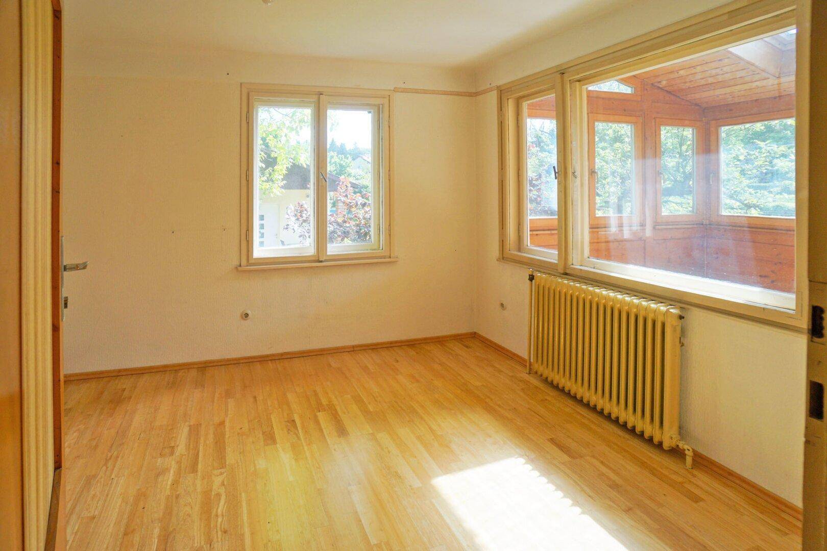 Helles Zimmer mit Parkettboden, großem Fenster und Zugang zum Wintergarten.