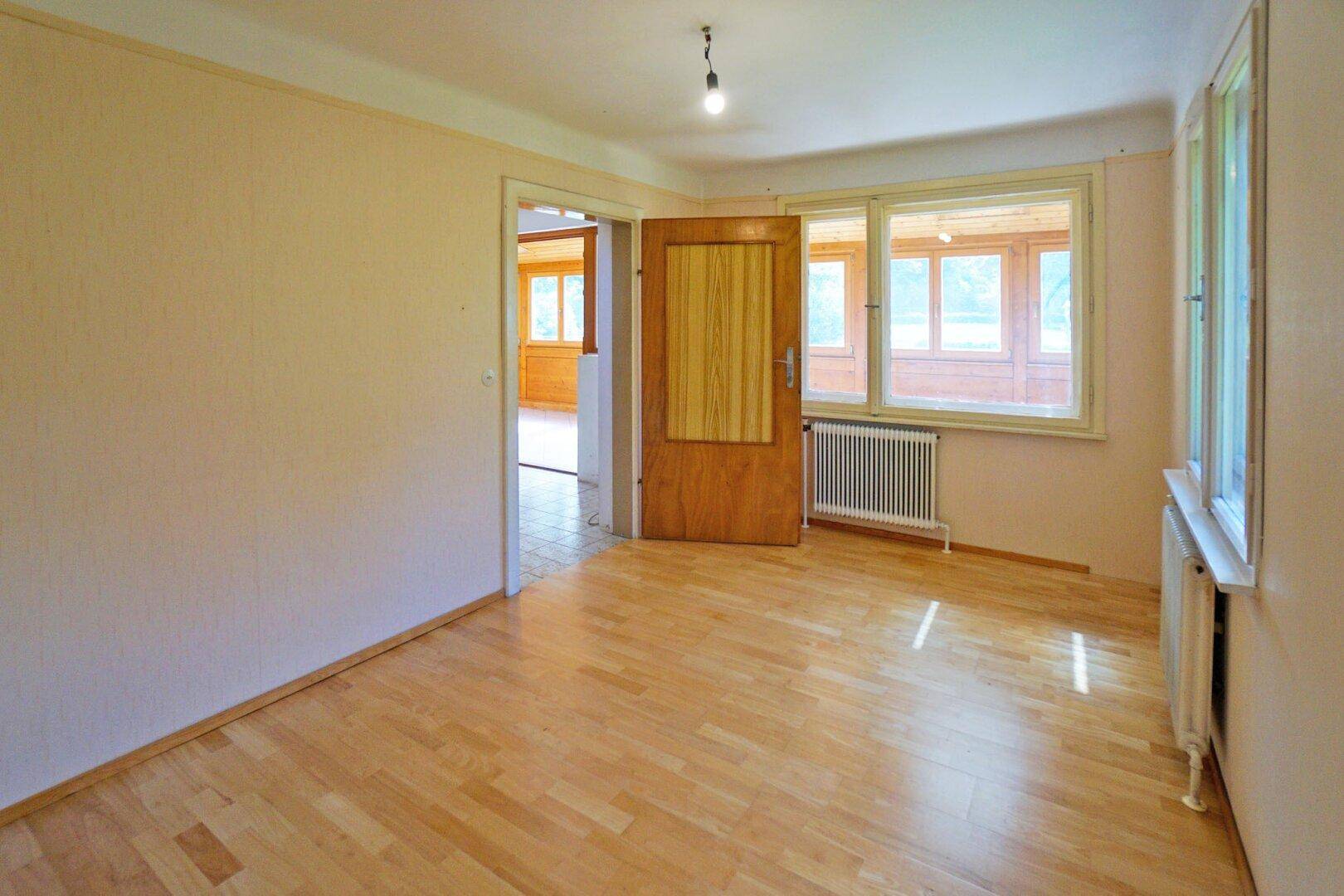 Geräumiges Zimmer mit Parkettboden, Heizkörper und Tür zum sonnigen Wintergarten.