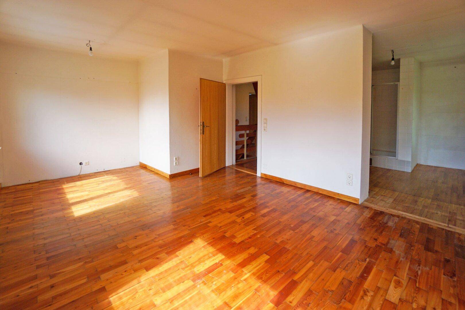 Großes, helles Zimmer mit Holzboden und viel Sonnenlicht, ideal zum Wohnen.
