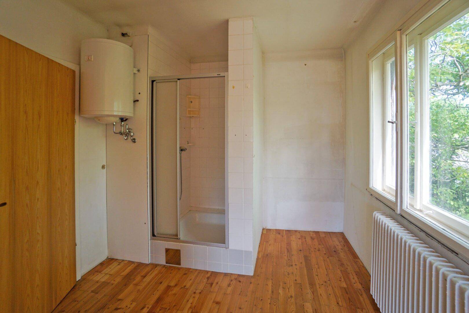 Badezimmer mit Duschkabine, Boiler und Fenster mit Blick ins Grüne.