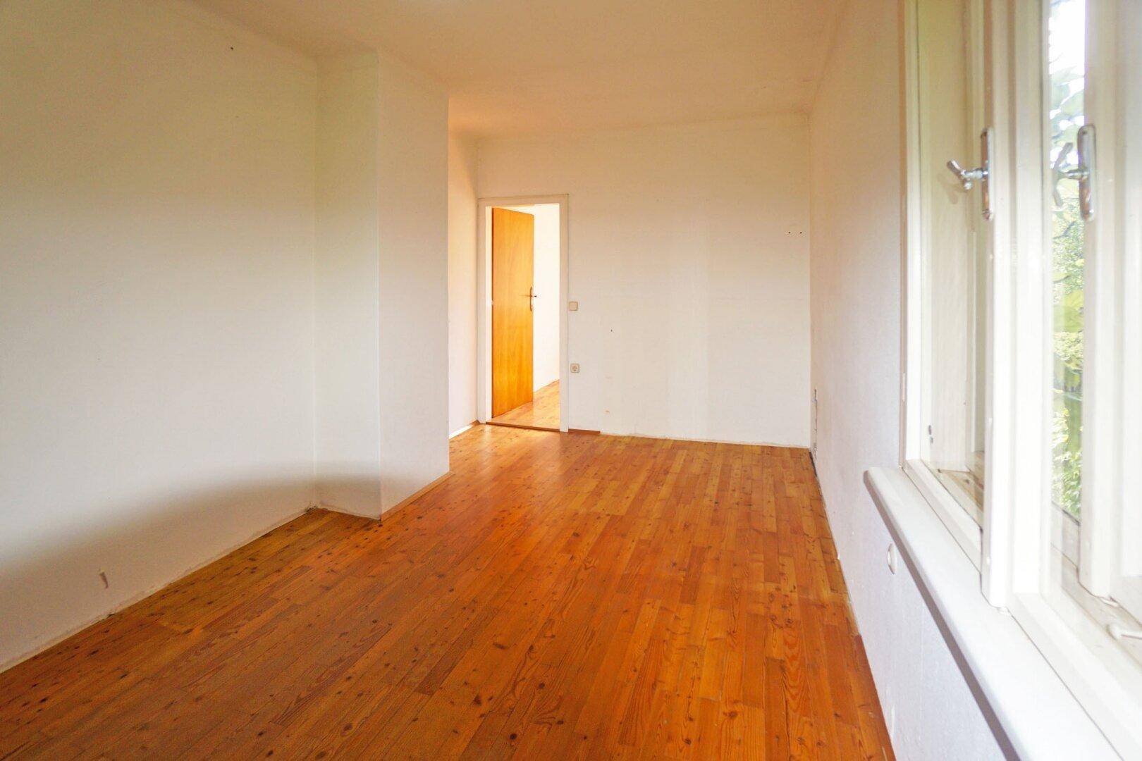 Helles Zimmer mit Holzboden und großem Fenster, ideal als Schlaf- oder Arbeitszimmer.