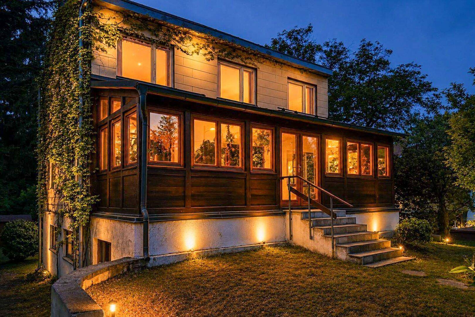 Das Haus bei Nacht, stimmungsvoll beleuchtet mit Gartenbeleuchtung und warmen Lichtern.