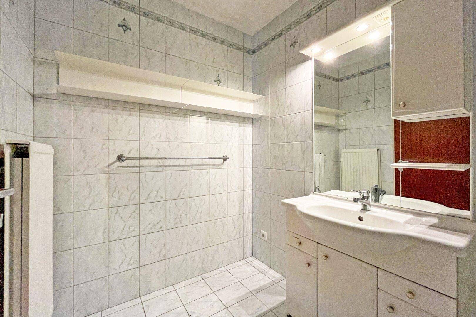 Badezimmer mit hellblauen Fliesen, einem Waschbeckenunterschrank und Spiegelschrank.