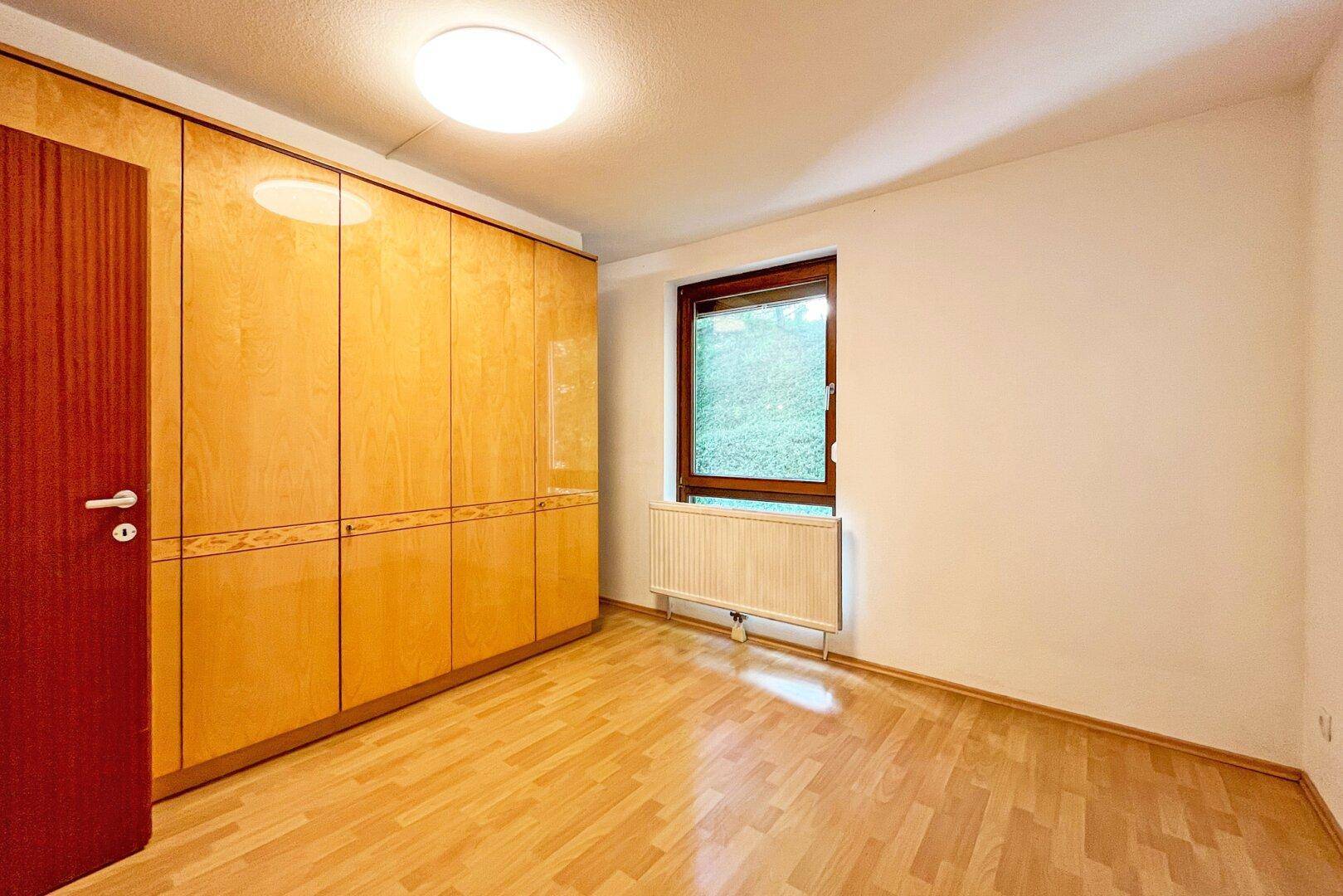Schlafzimmer mit Laminatboden, großem Einbauschrank und Fenster mit Blick ins Grüne.