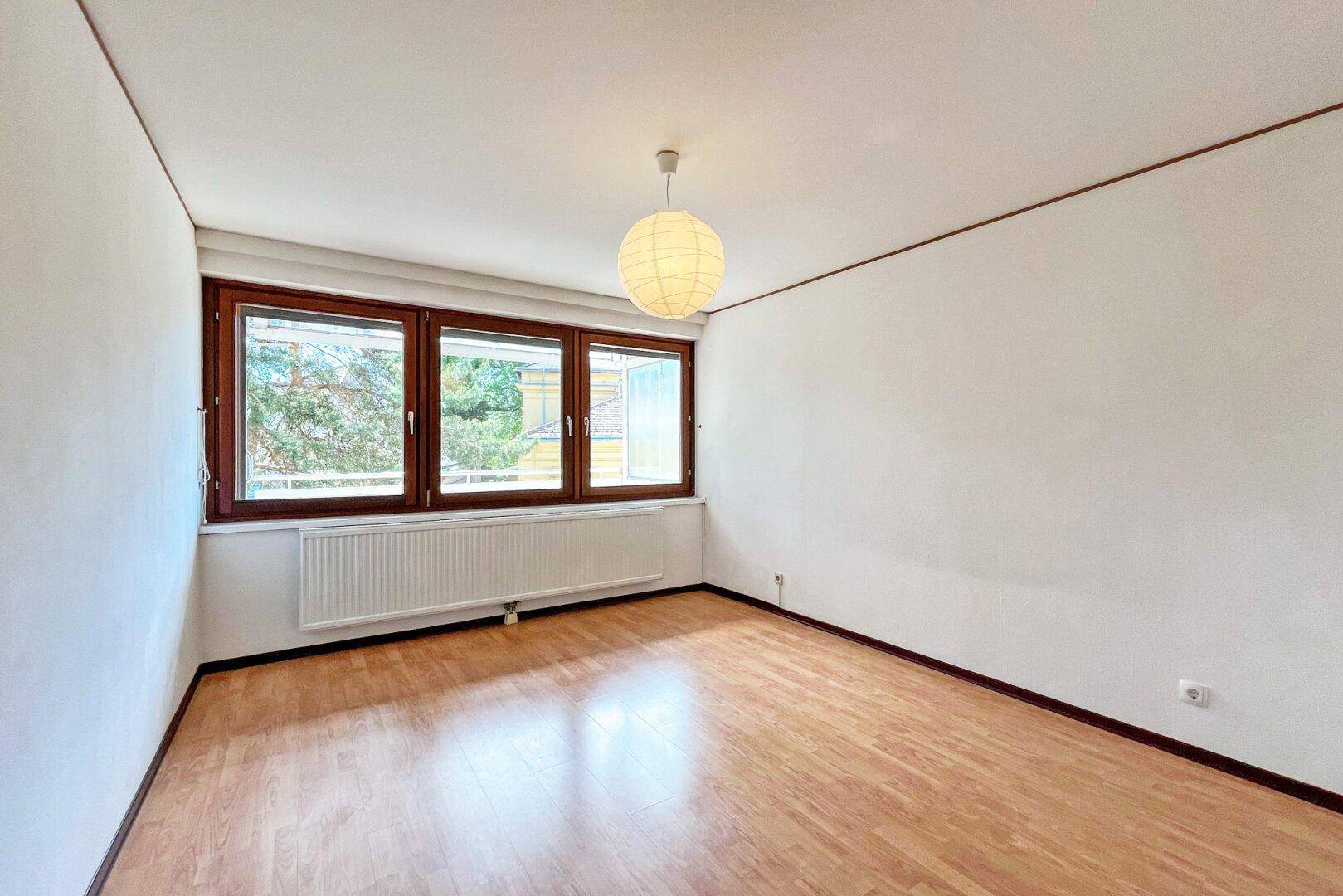 Helles Zimmer mit Laminatboden und großen Fenstern, die viel Tageslicht hereinlassen.