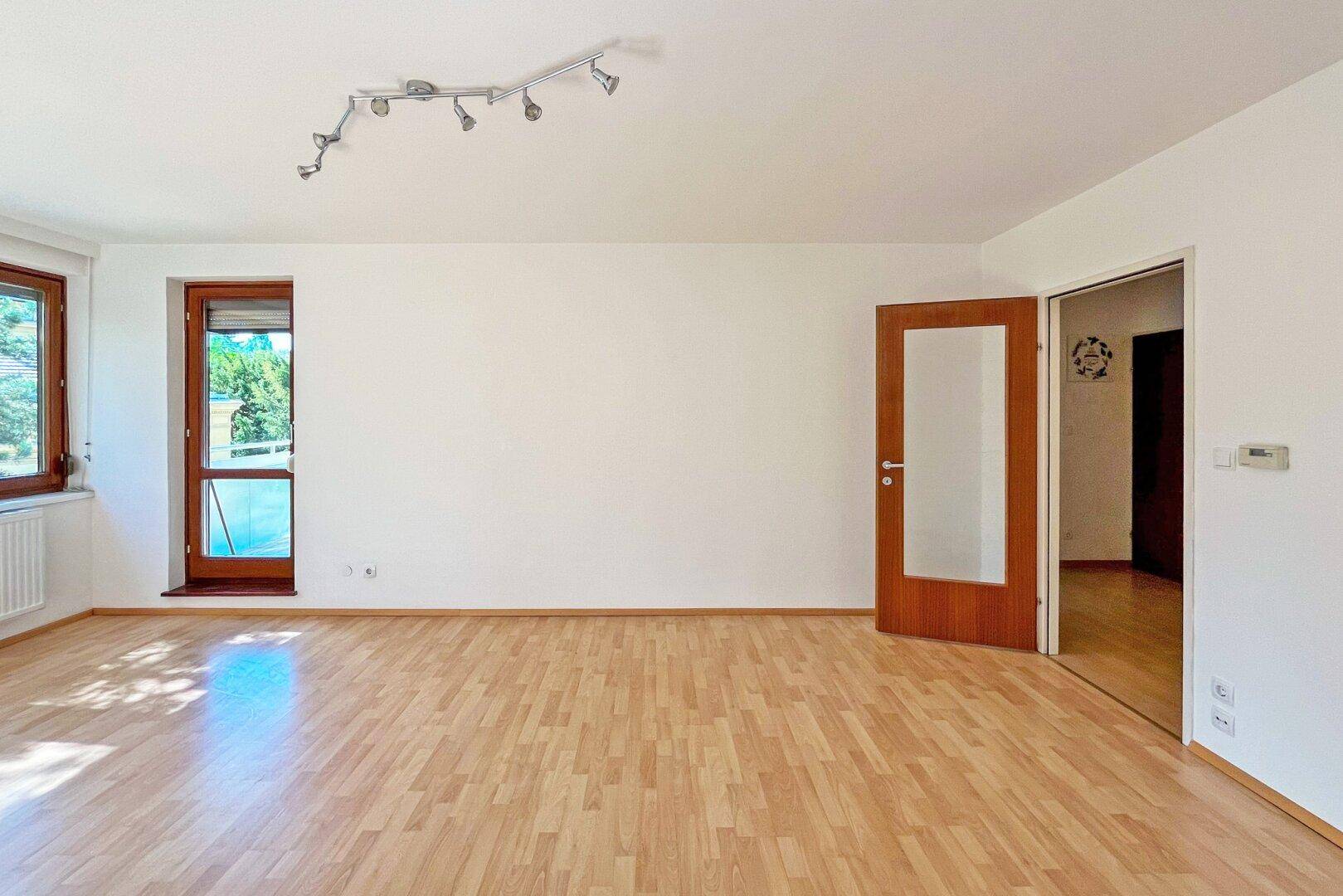 Geräumiges Wohnzimmer mit Laminatboden und Zugang zu einem Balkon, hell und einladend.