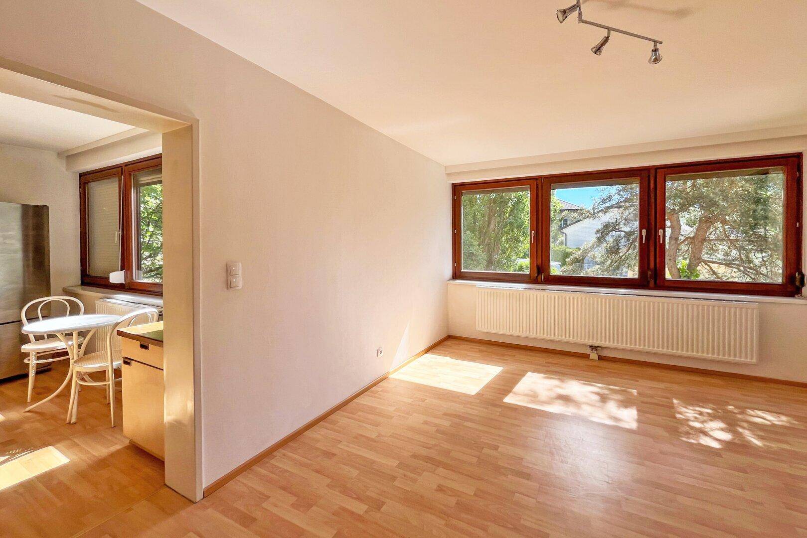 Heller Wohnbereich mit Laminatboden und großen Fenstern, angrenzend an die Küche.