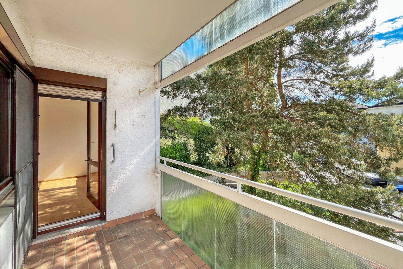 Balkon mit Fliesenboden und Blick auf Bäume sowie die darunterliegende Straße.