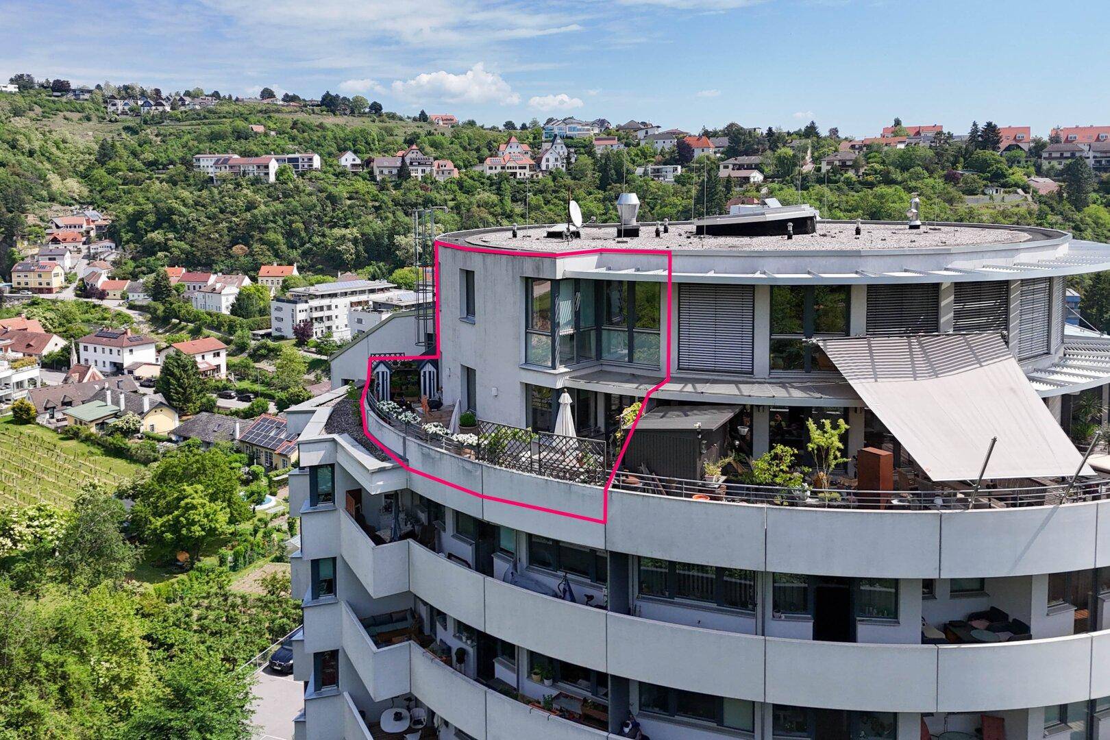 Luftaufnahme eines modernen, runden Apartmentgebäudes mit Terrassen und Blick auf die hügelige Landschaft.