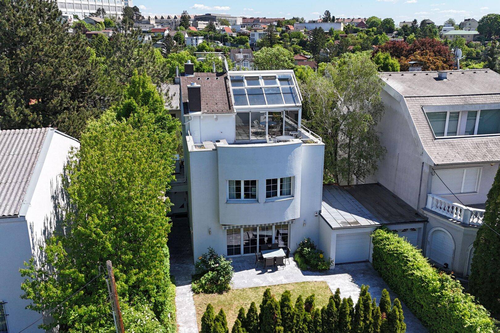 Luftaufnahme der modernen Villa mit Wintergarten, Garten und umliegender Wohnbebauung.