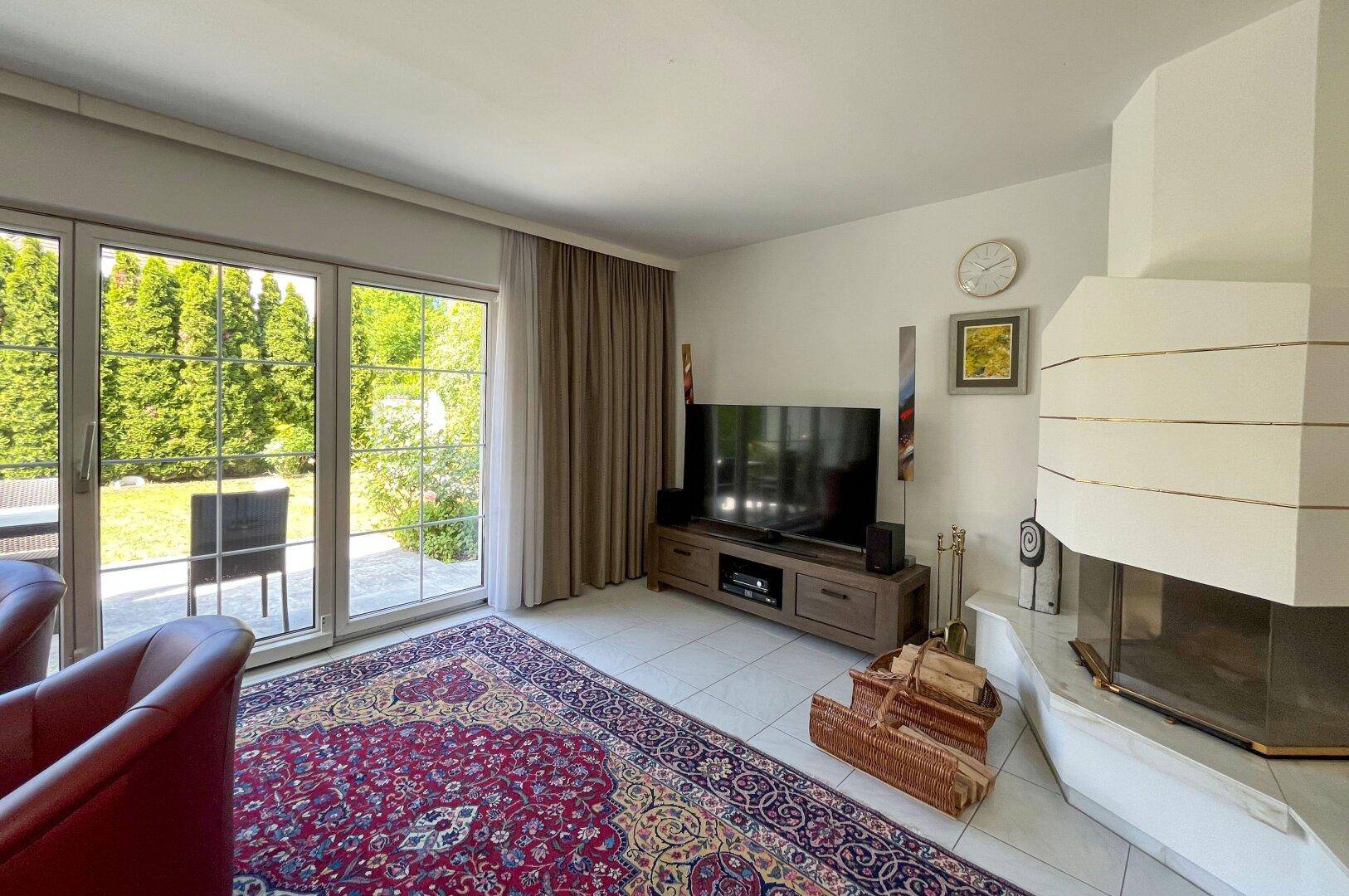 Gemütliches Wohnzimmer mit Kamin, Fliesenboden und direktem Zugang zum Garten.