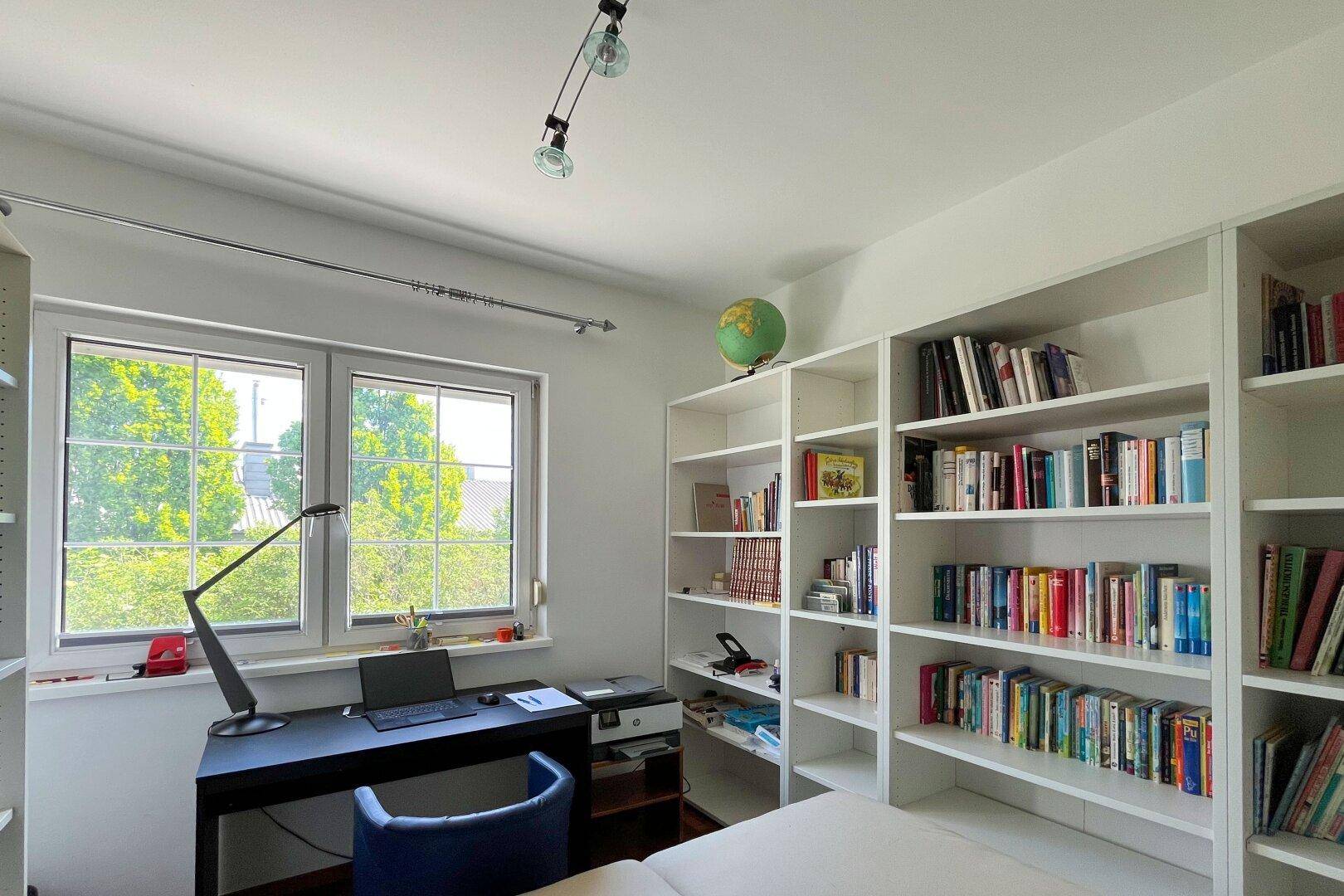 Helles Arbeitszimmer mit großem Fenster, Schreibtisch und integrierten Bücherregalen.