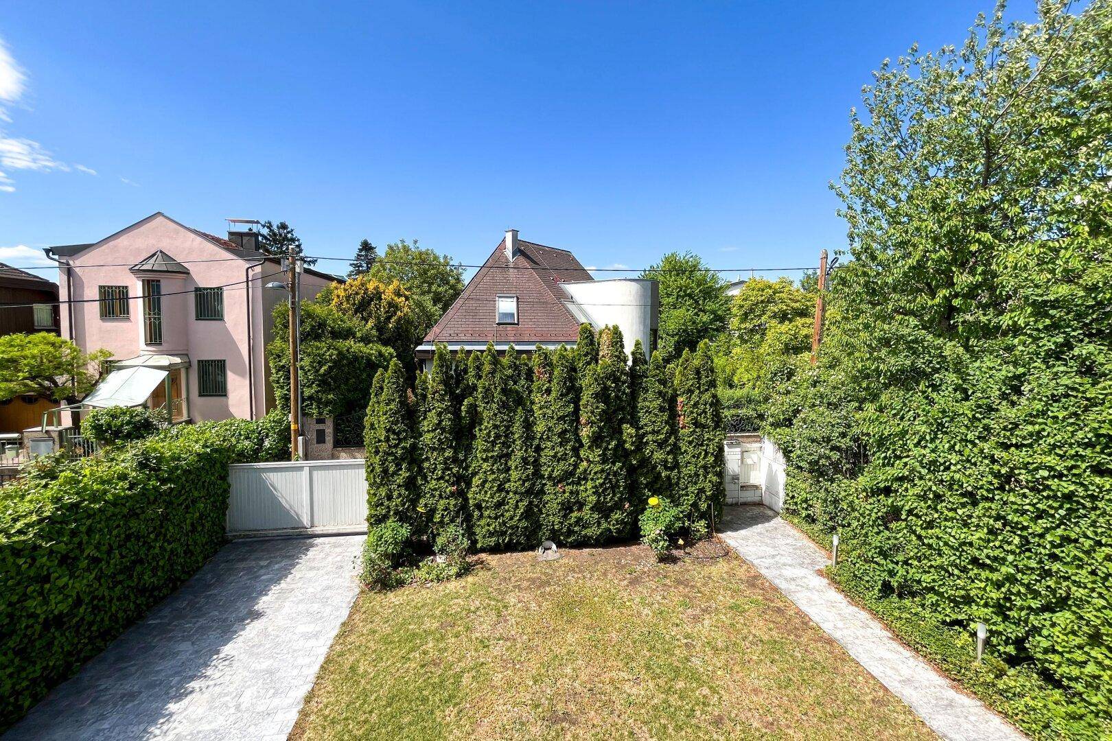 Gepflegter Garten mit Rasen, hohen Hecken und Zufahrtstor zur Immobilie.