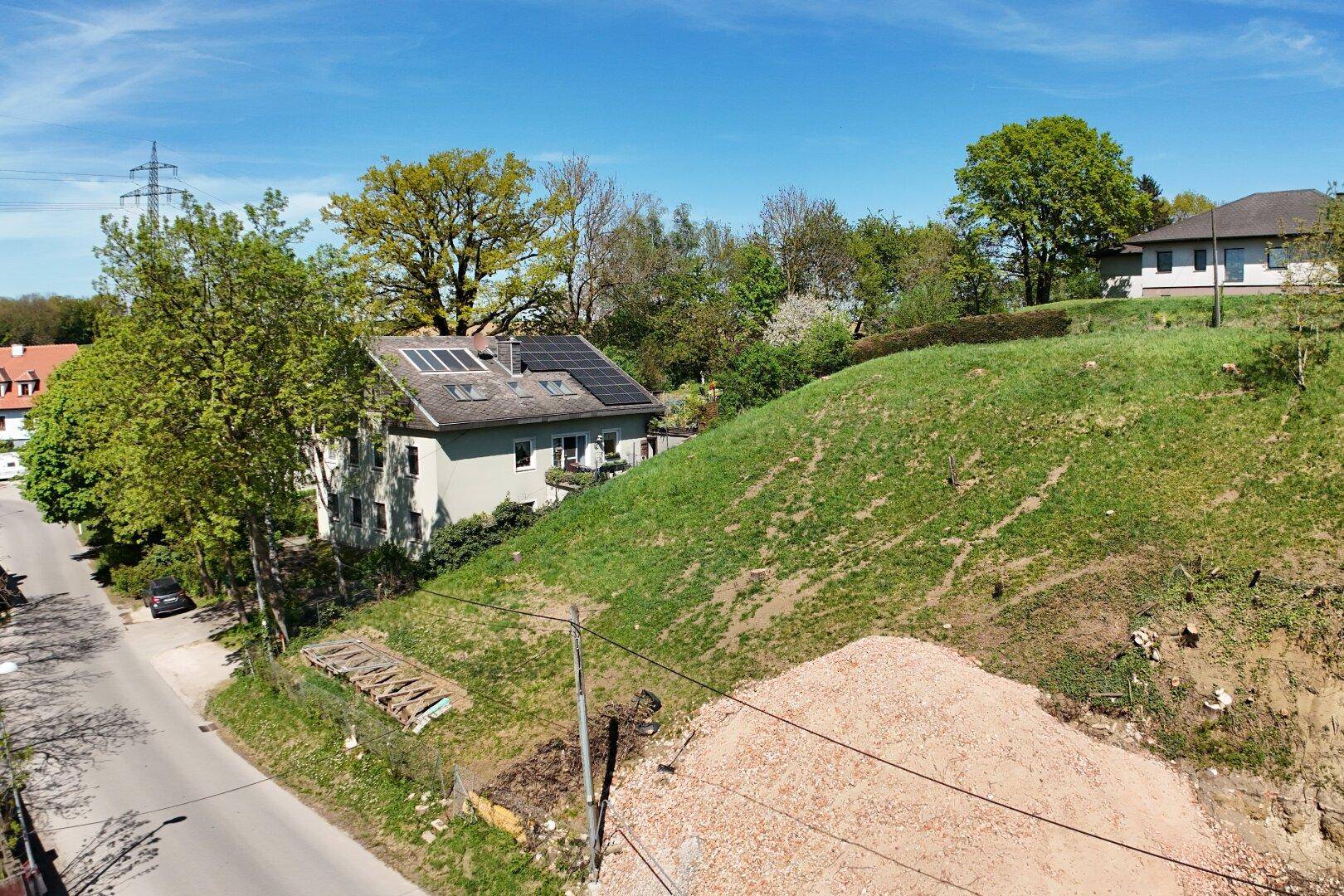 Blick auf eine Wohnstraße, ein Haus mit Solaranlage und eine begrünte Hanglage.