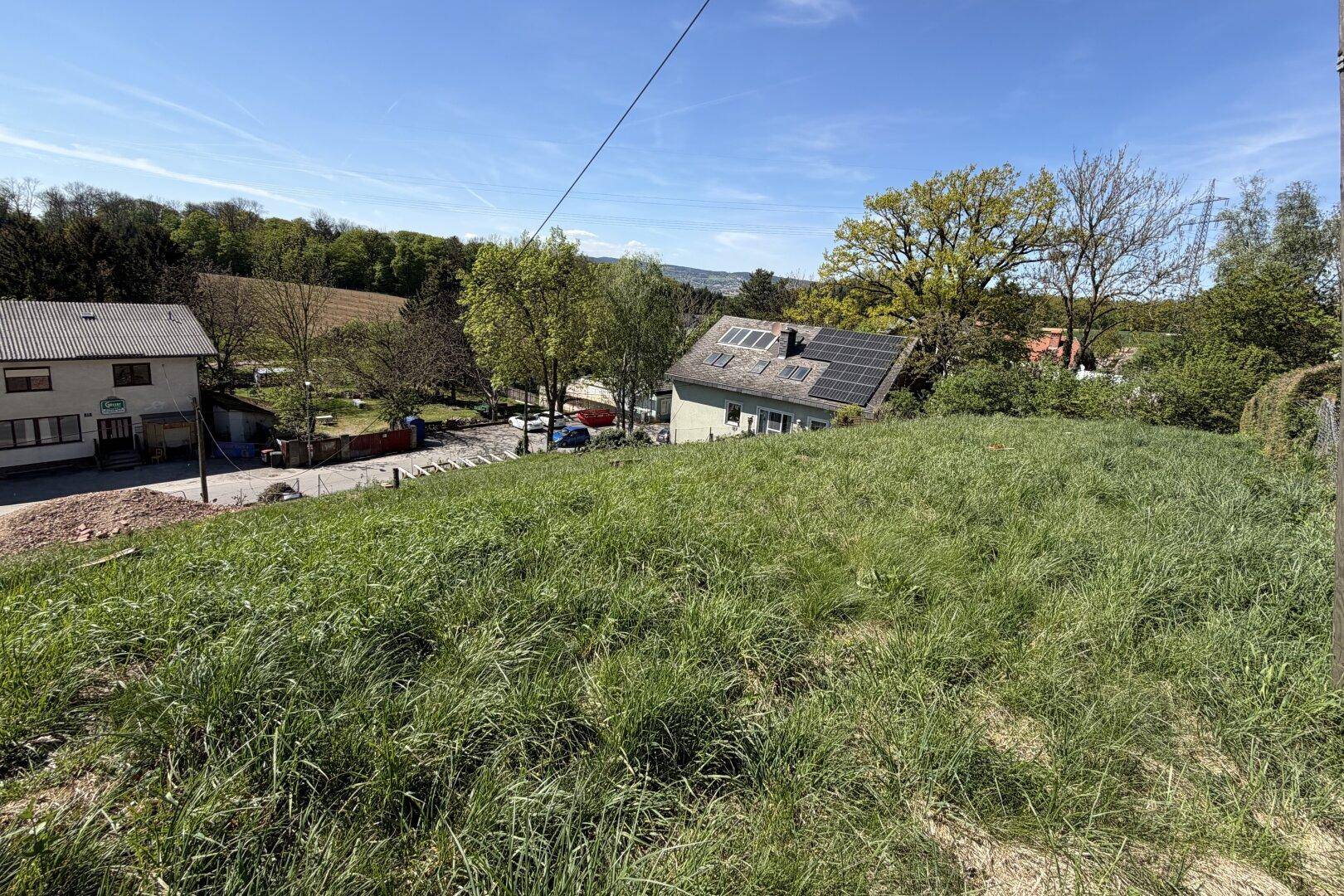 Aussicht von einem Grashügel auf Wohnhäuser, eine Straße und die umliegende Landschaft.