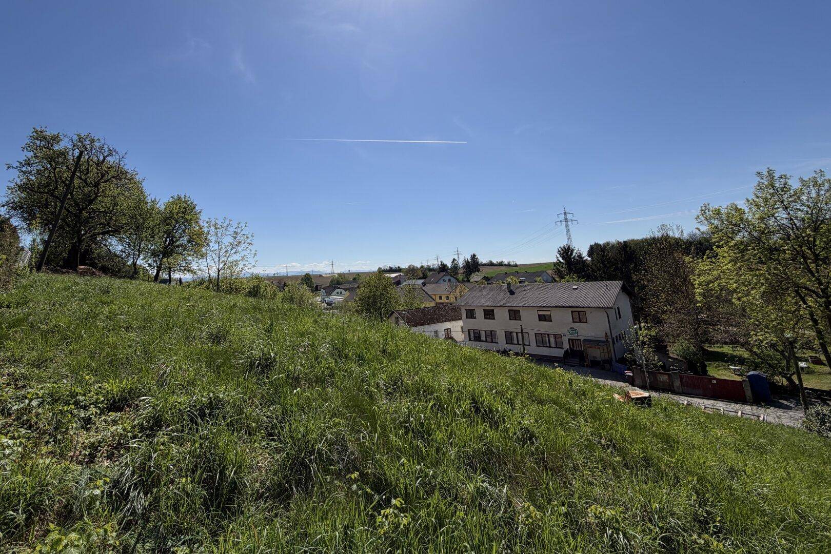 Panoramablick von einem Grashang auf eine ländliche Siedlung und weite Felder.