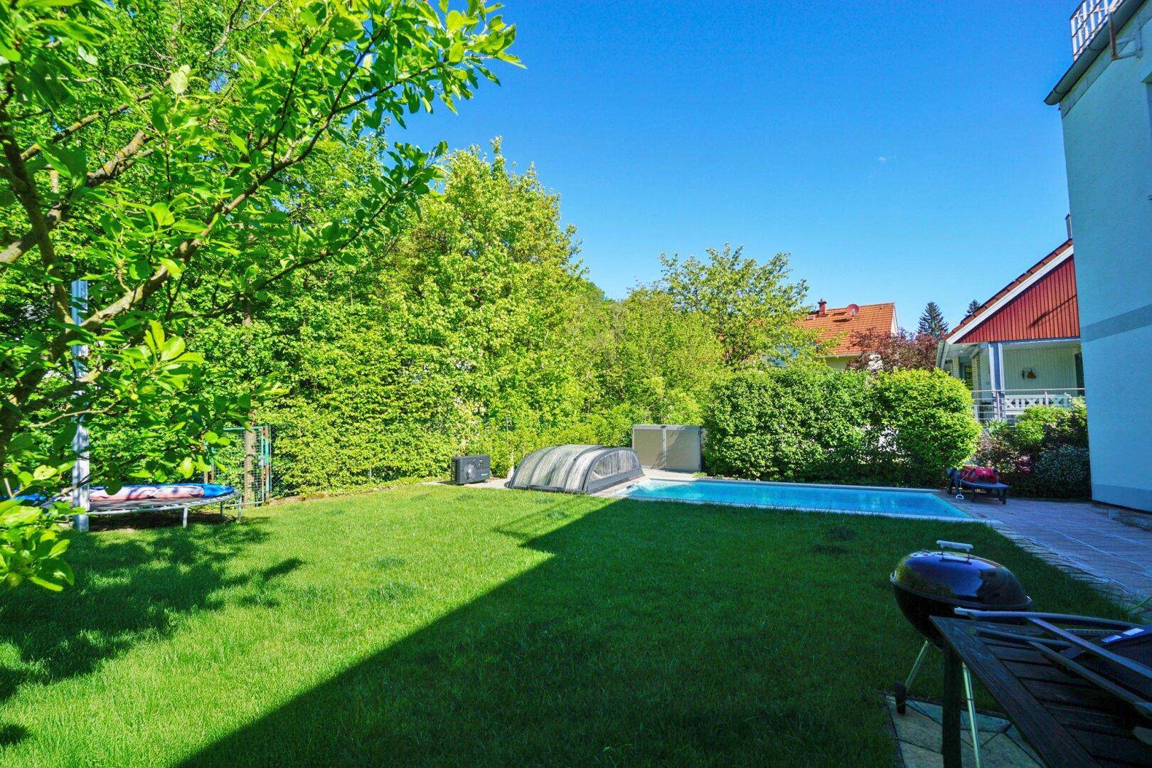 Gepflegter Gartenbereich mit Rasenfläche, Pool und Grillplatz, umgeben von Hecken.