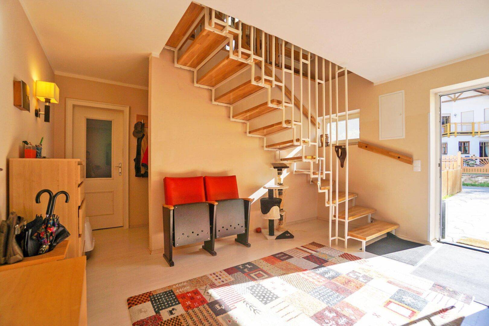 Heller Eingangsbereich mit moderner Holztreppe und gemustertem Teppich.
