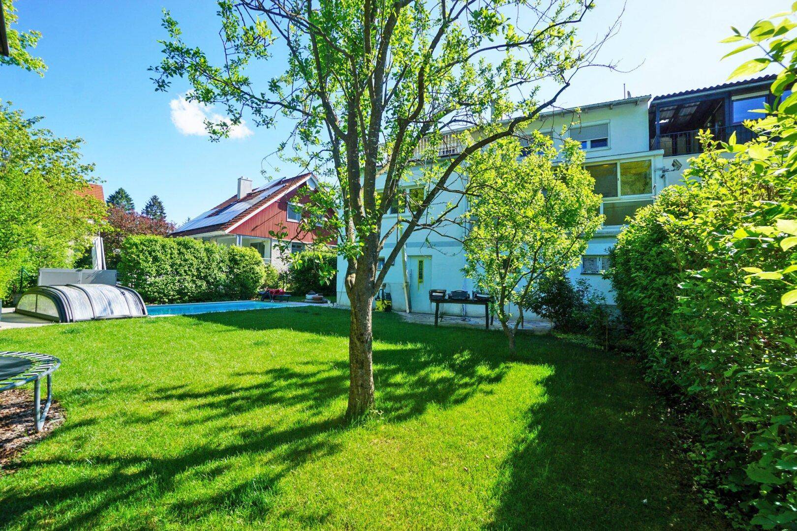 Weitläufiger Garten mit Rasen, Bäumen und Blick auf das Haus mit Poolbereich.