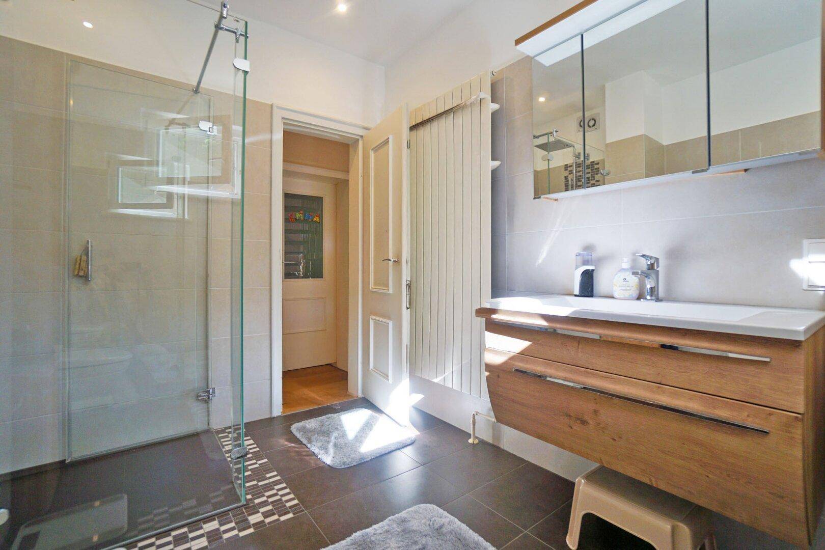 Modernes Badezimmer mit begehbarer Dusche, Holzwaschtisch und Spiegelschrank.