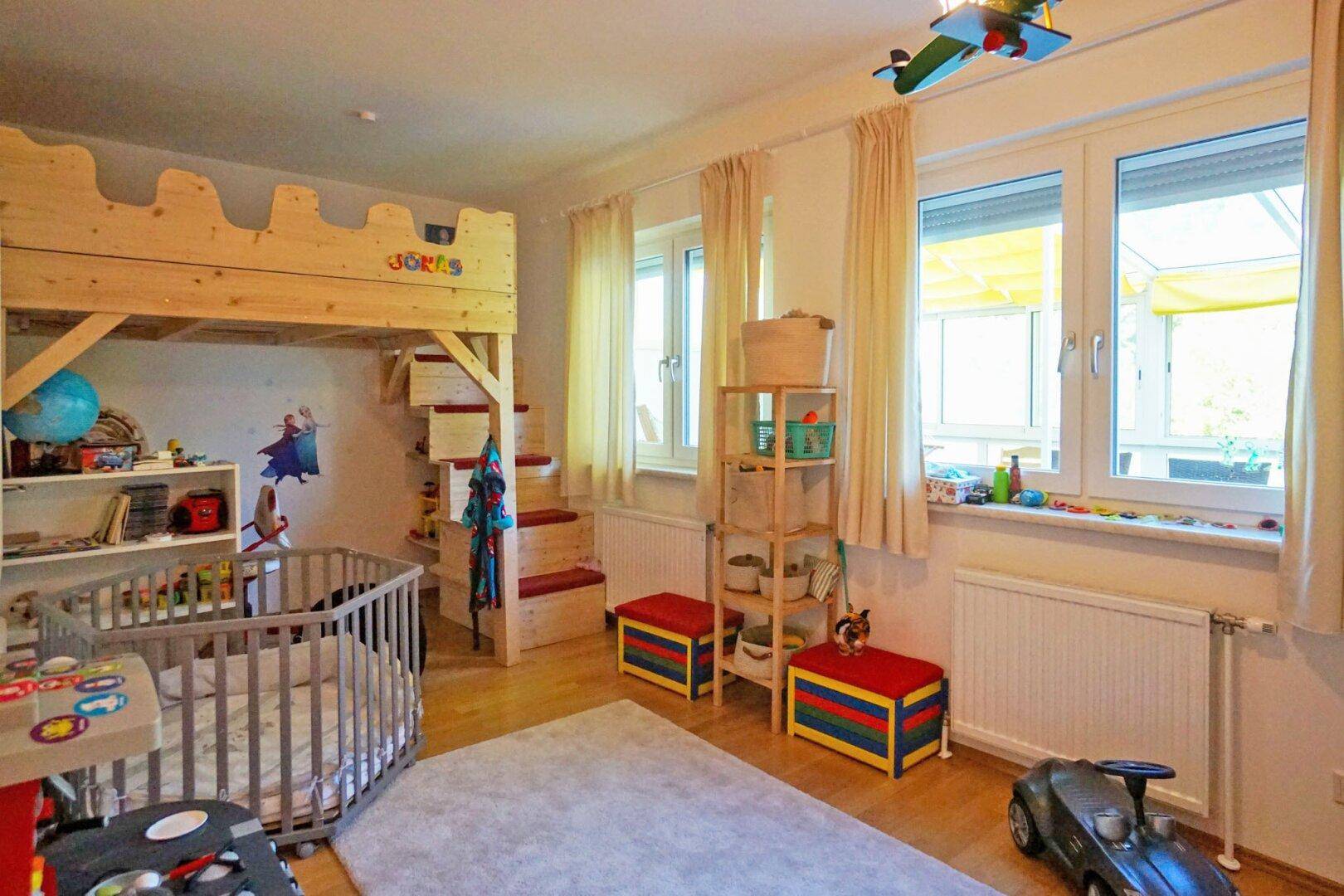 Kinderzimmer mit Hochbett, Babybett und Spielzeug, hell und freundlich gestaltet.