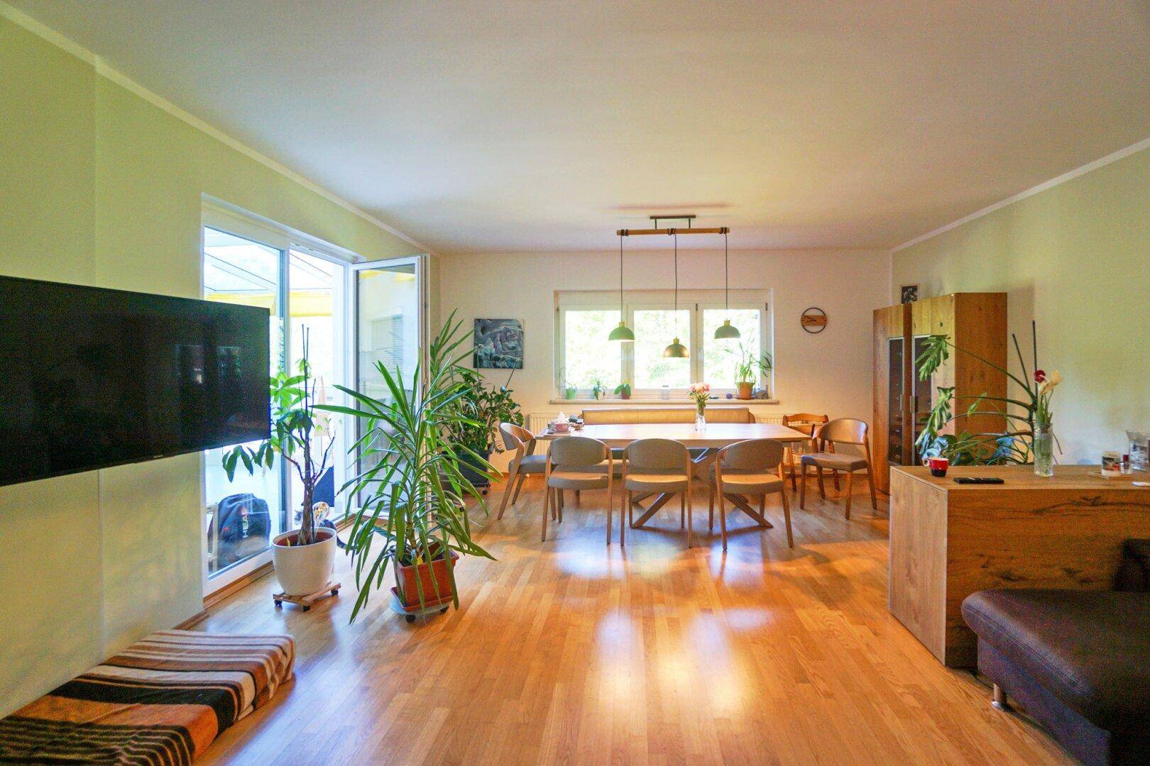 Geräumiger Wohn-Essbereich mit Holzboden, großem Esstisch und Zugang zur Terrasse.
