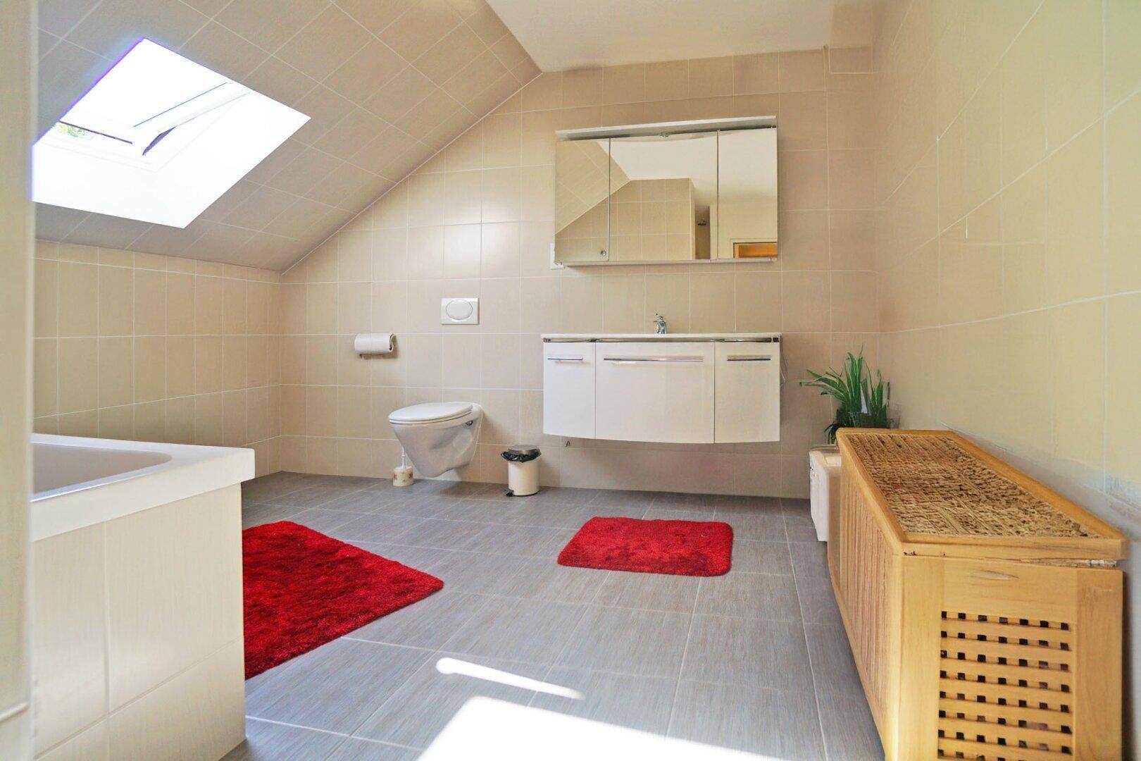 Modernes Badezimmer im Dachgeschoss mit Badewanne, WC und Spiegelschrank.