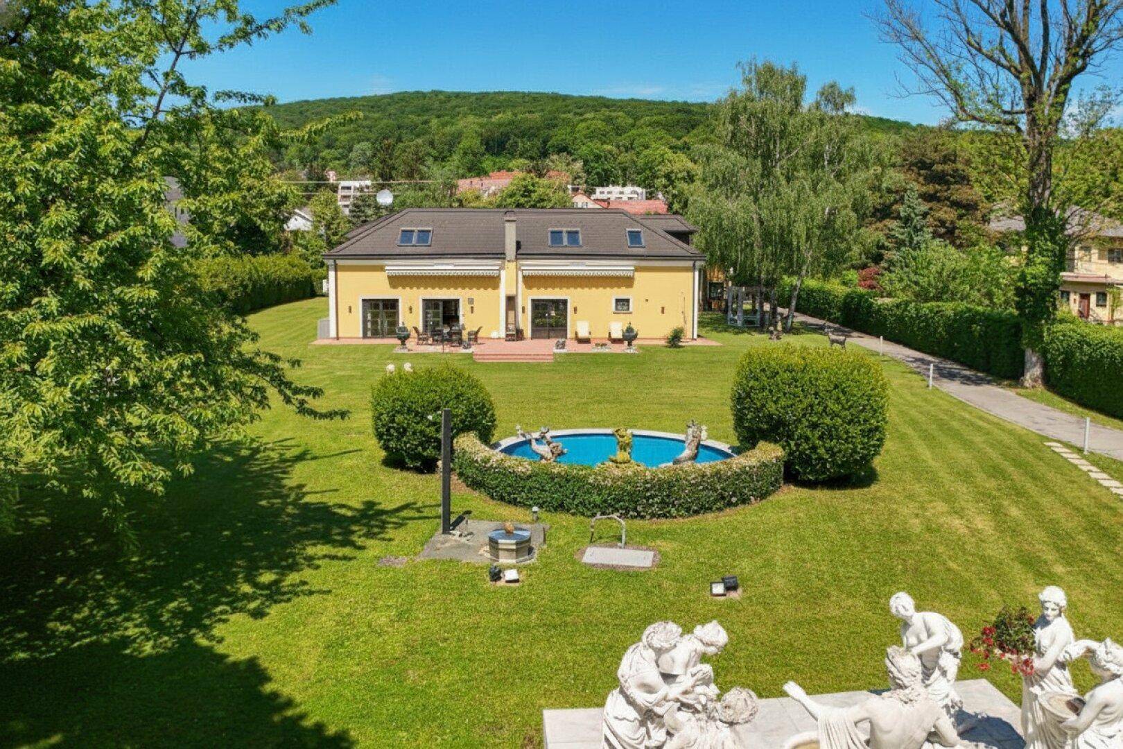 Weitläufiger Garten mit großem Rasen, dekorativem Brunnen und Blick auf die bewaldeten Hügel.
