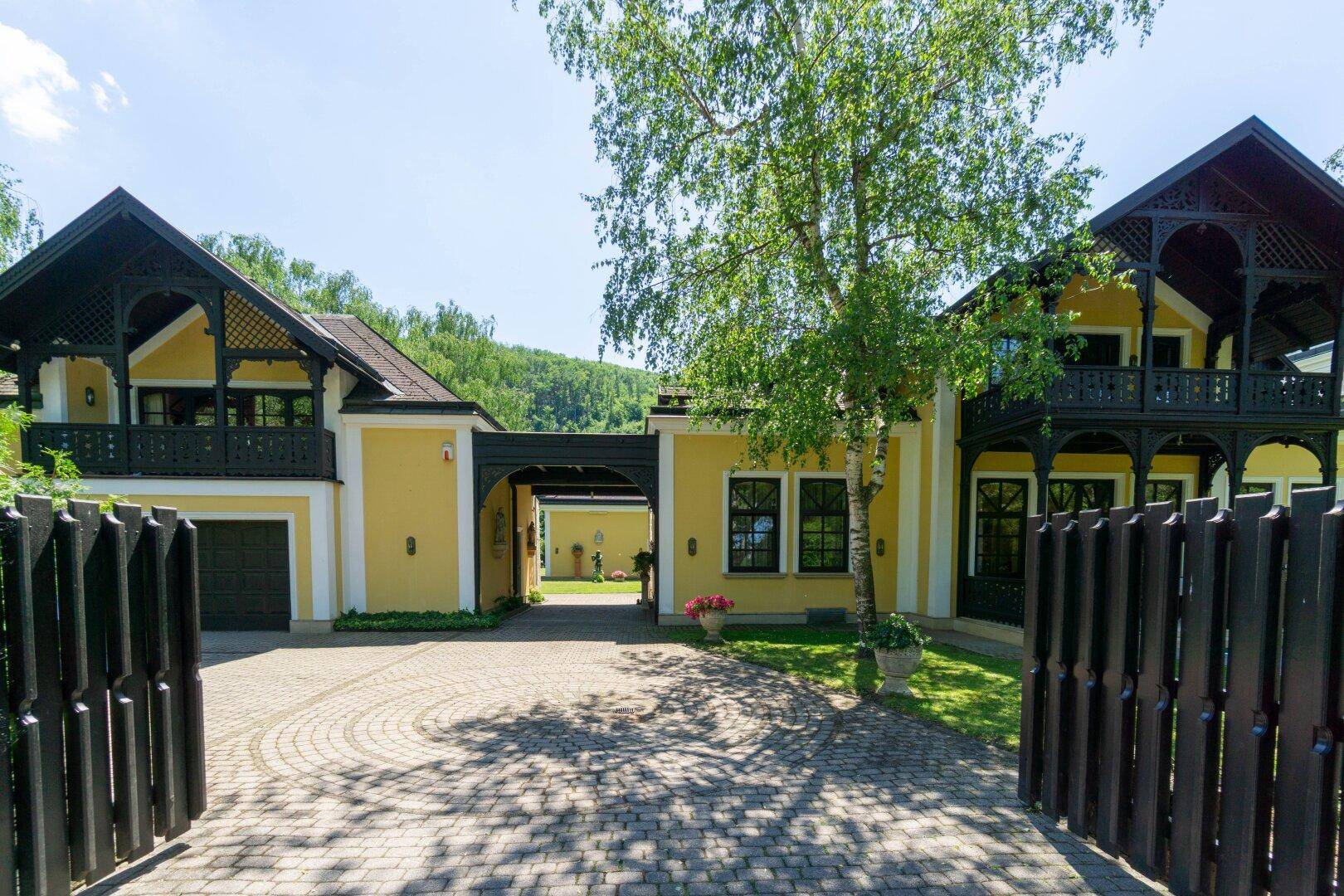 Einfahrt zum Anwesen mit gepflastertem Weg, schmiedeeisernem Tor und traditioneller Architektur.