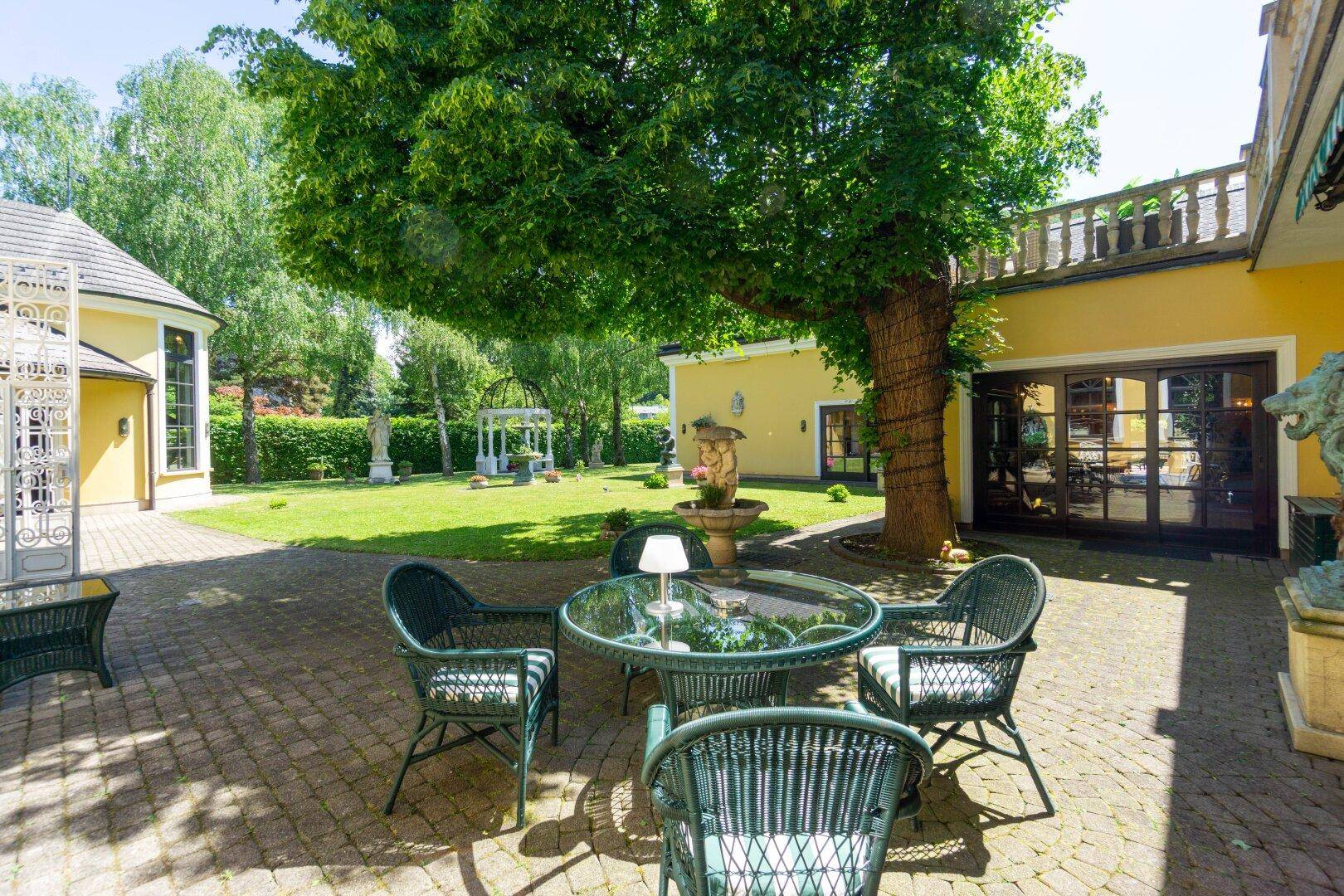 Gemütliche Terrasse mit Korbmöbeln unter einem großen Baum, ideal für entspannte Stunden im Freien.