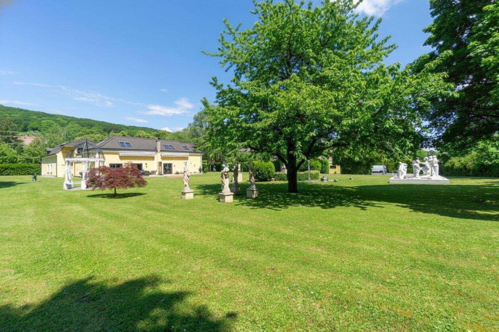 Weitläufiger Parkgarten mit großen Rasenflächen, alten Bäumen und klassischen Statuen.