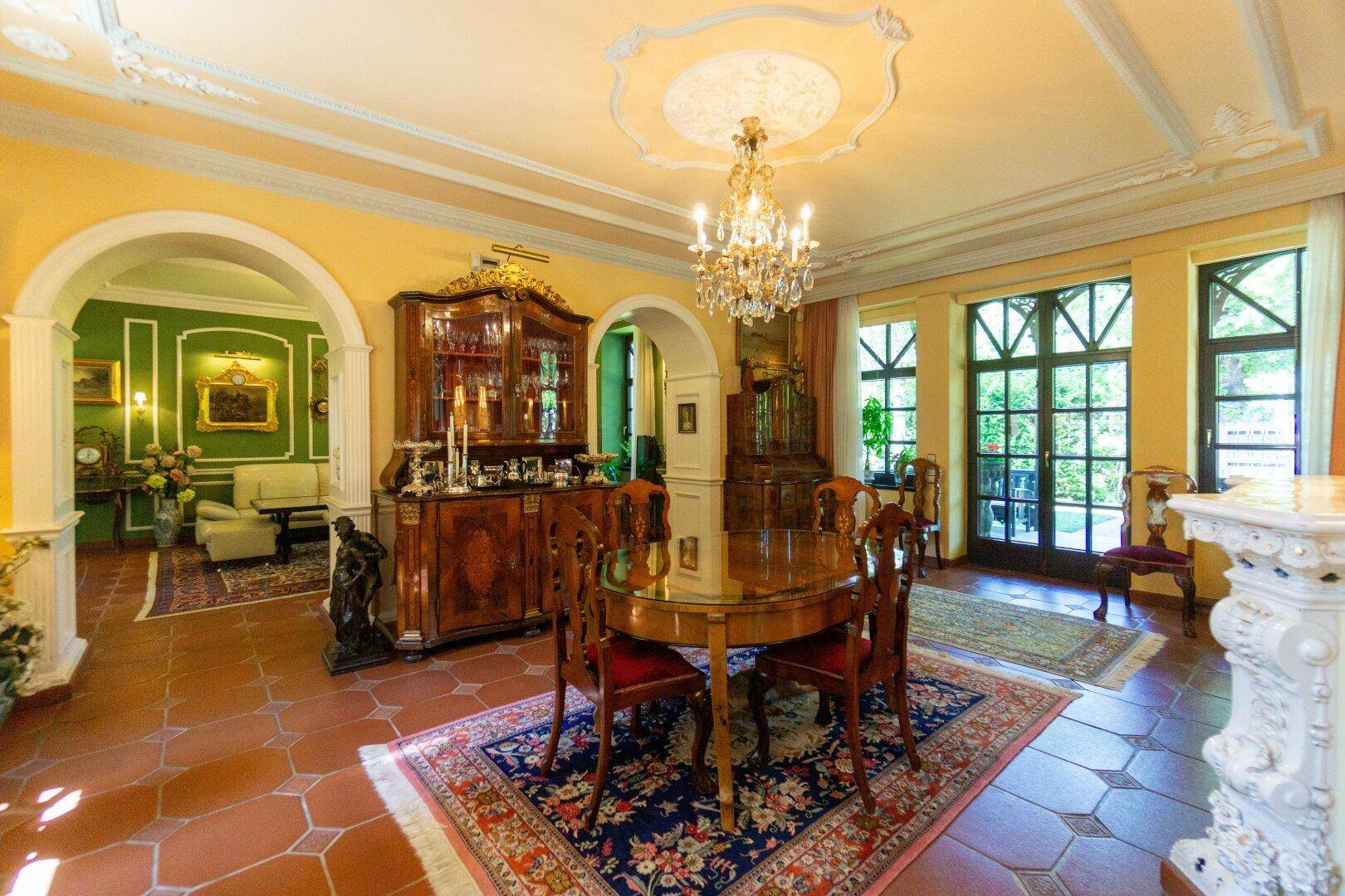 Elegantes Esszimmer mit Terrakottaboden, Kronleuchter und Zugang zu einem angrenzenden Wohnbereich.