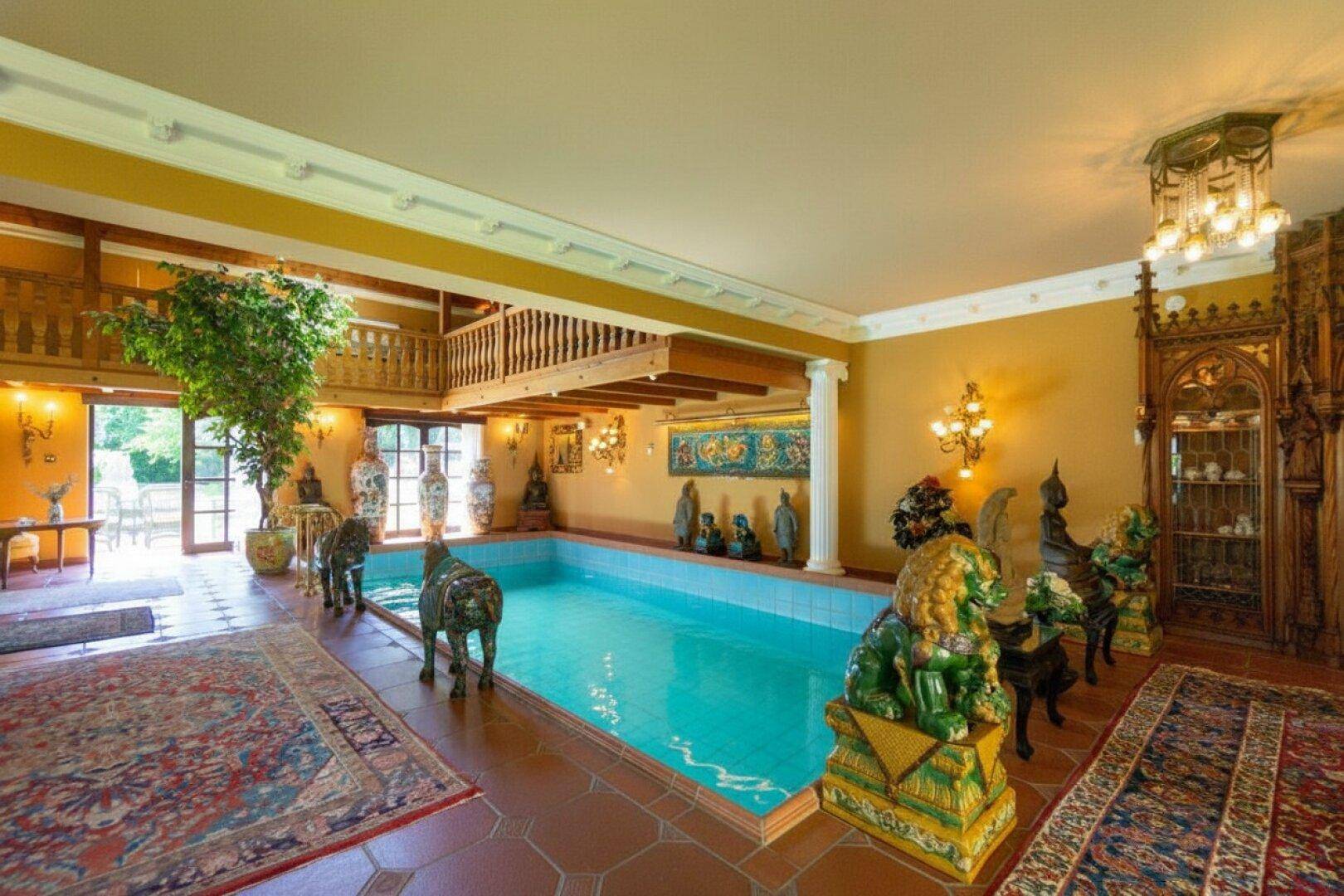 Exklusiver Innenpoolbereich mit kunstvollen Dekorationen, hohen Decken und Zugang zum Garten.