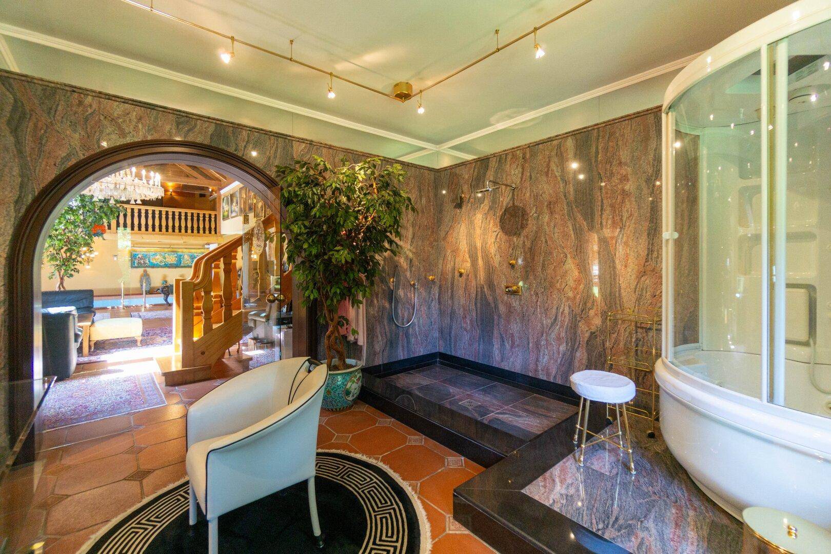 Luxuriöses Badezimmer mit Marmorwänden, großer Dusche und Zugang zum Poolbereich.