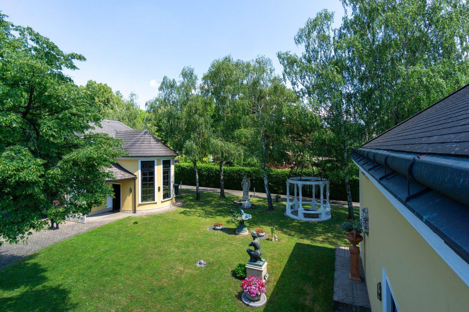 Panoramablick auf den weitläufigen Garten mit Rasenflächen, Bäumen und einem dekorativen Pavillon.