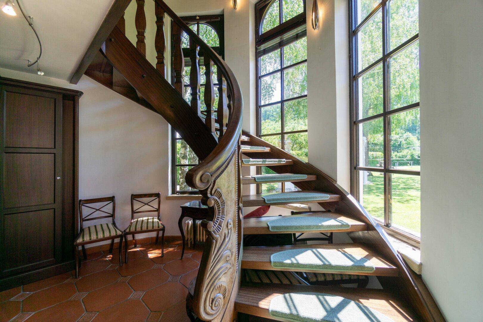 Elegante Holztreppe mit großen Fenstern, die viel natürliches Licht hereinlassen und den Garten zeigen.