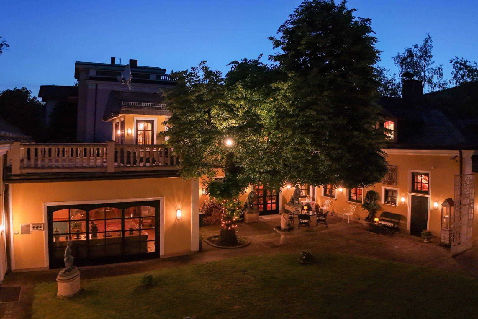Stimmungsvoll beleuchteter Innenhof mit Rasen, Bäumen und dekorativen Elementen in der Nacht.