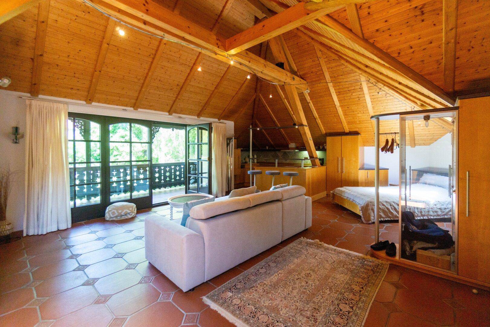 Gemütlicher Dachgeschoss-Wohnbereich mit Holzbalken, Terrakottaboden und Zugang zum Balkon.