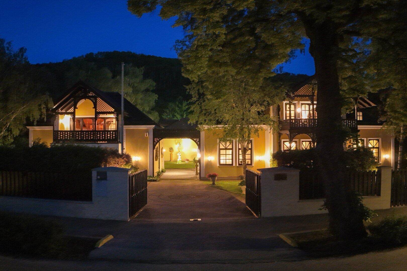 Eindrucksvolle Villa bei Nacht mit beleuchtetem Eingangsbereich und gepflegter Gartenanlage.