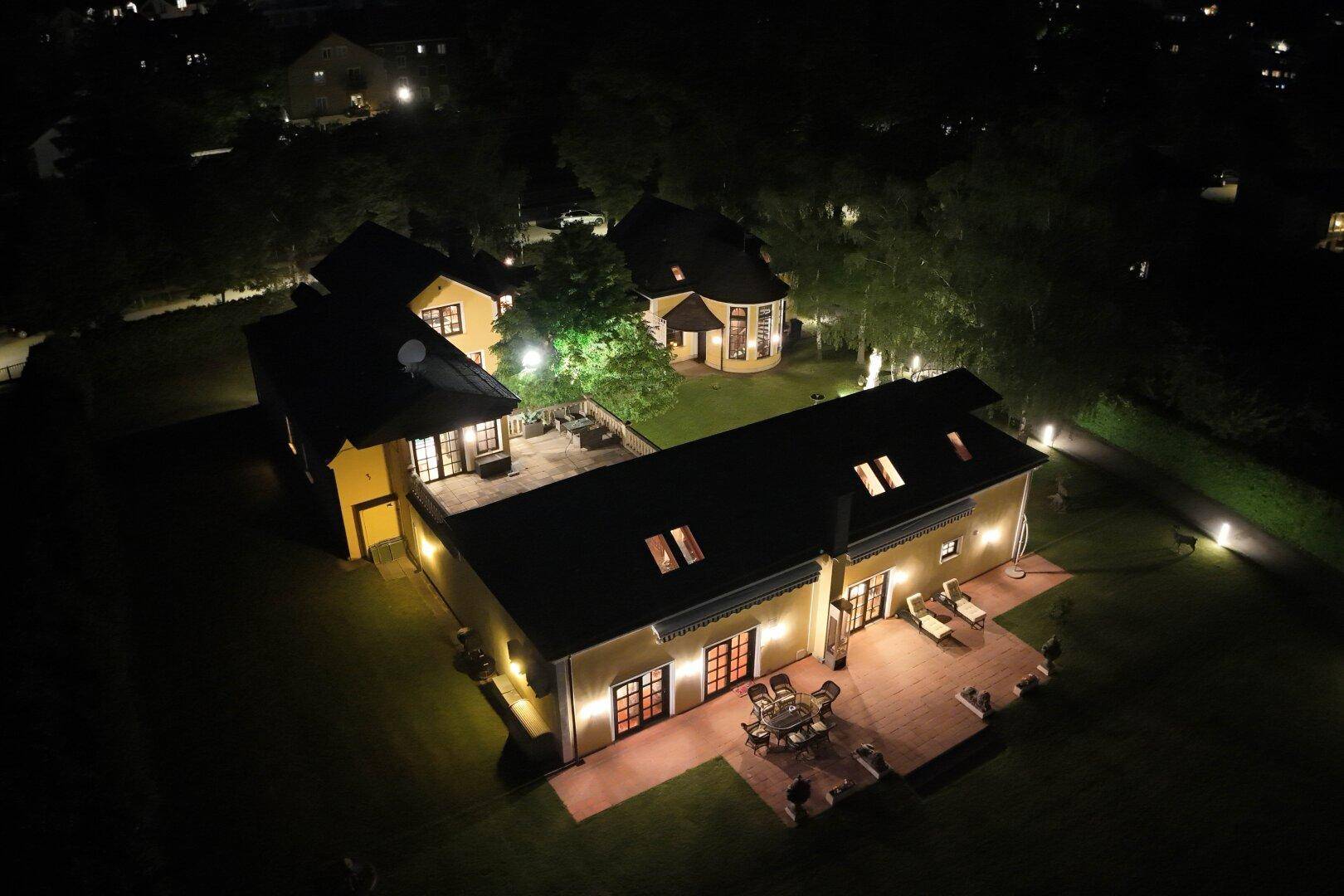 Luftaufnahme der weitläufigen Villa bei Nacht mit mehreren Gebäuden und großer Terrasse.