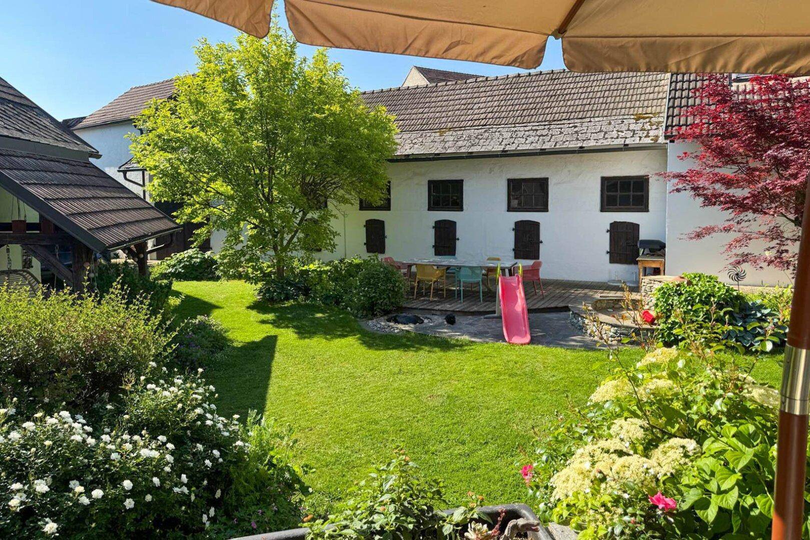 Sonniger Garten mit Terrasse, Esstisch im Freien und einer Kinderrutsche.