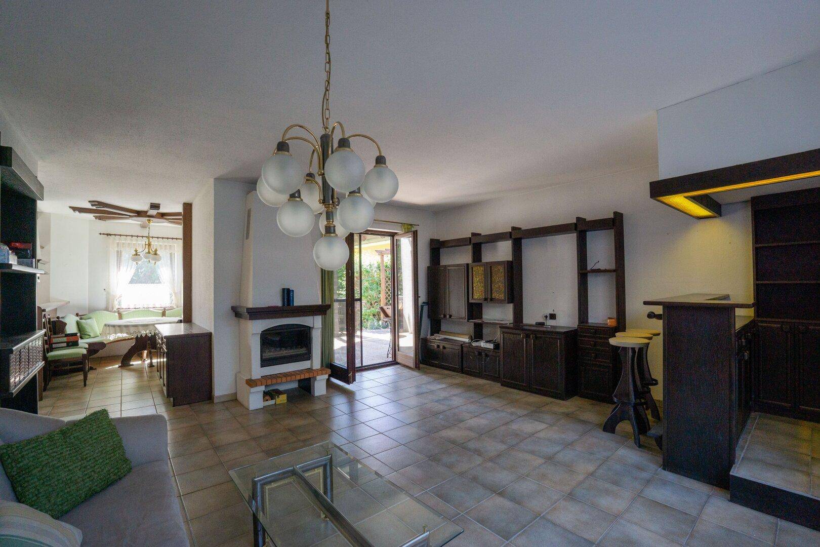 Geräumiges Wohnzimmer mit Kamin, gefliestem Boden und Zugang zur Terrasse, inklusive Barbereich.