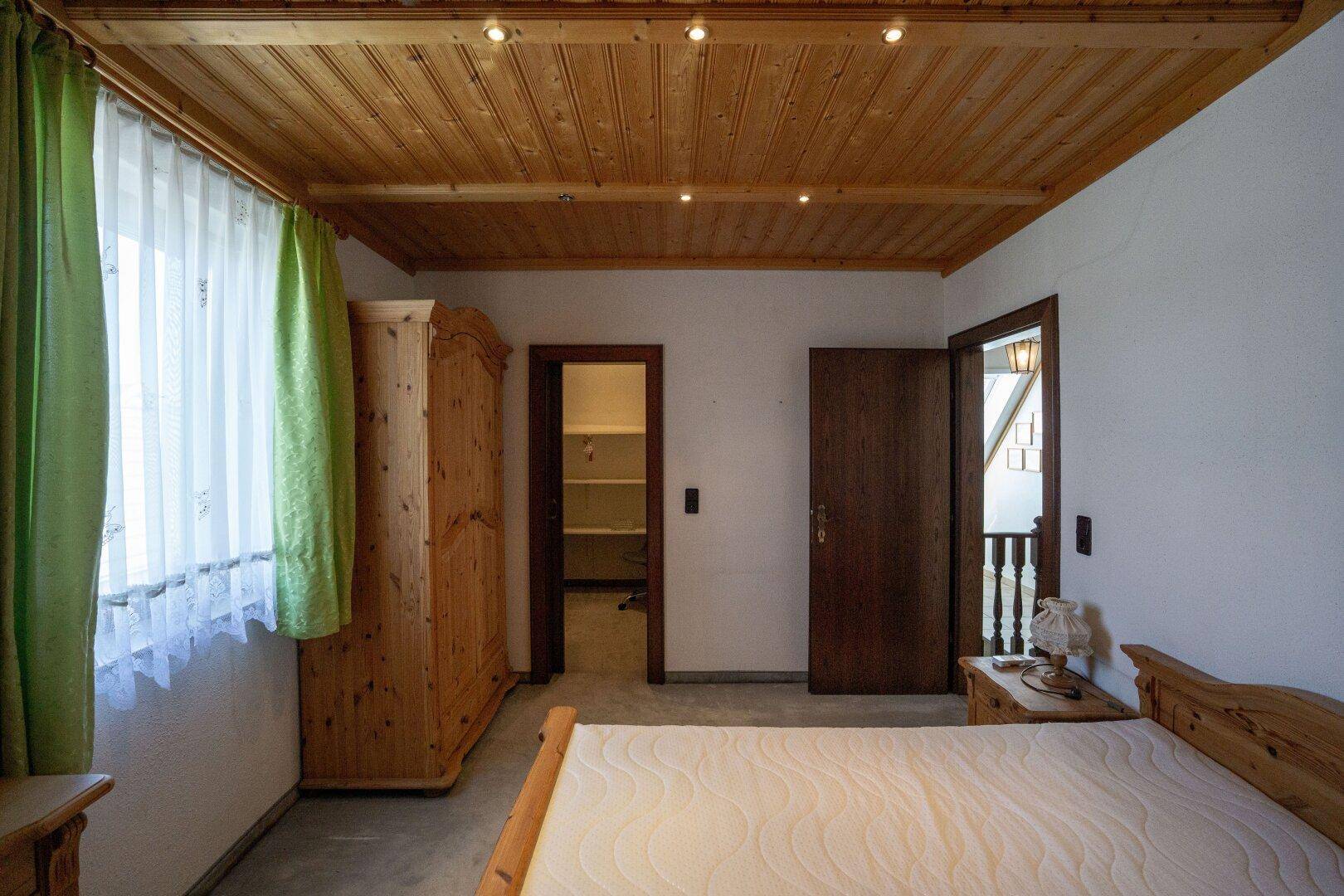 Gemütliches Schlafzimmer mit Holzdecke, Holzbett und Kleiderschrank, hell durch Tageslicht.