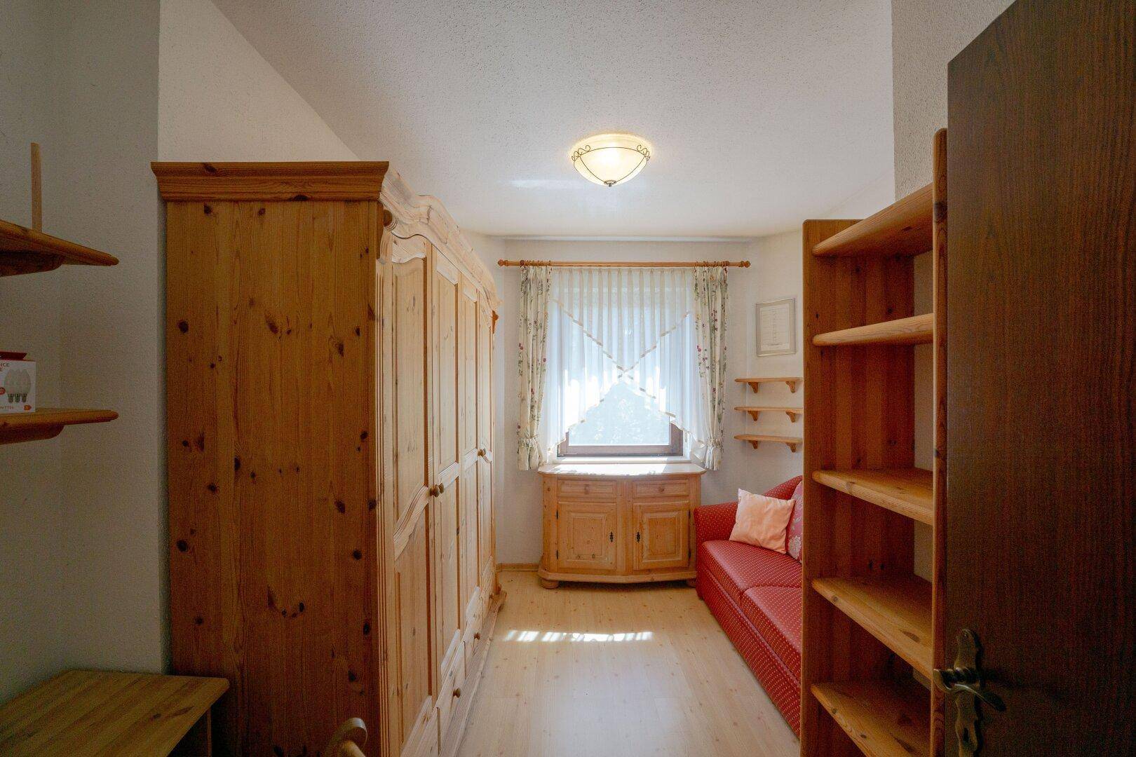 Helles Schlafzimmer mit Holzmöbeln, rotem Sofa und Fenster mit Vorhängen, einladend gestaltet.
