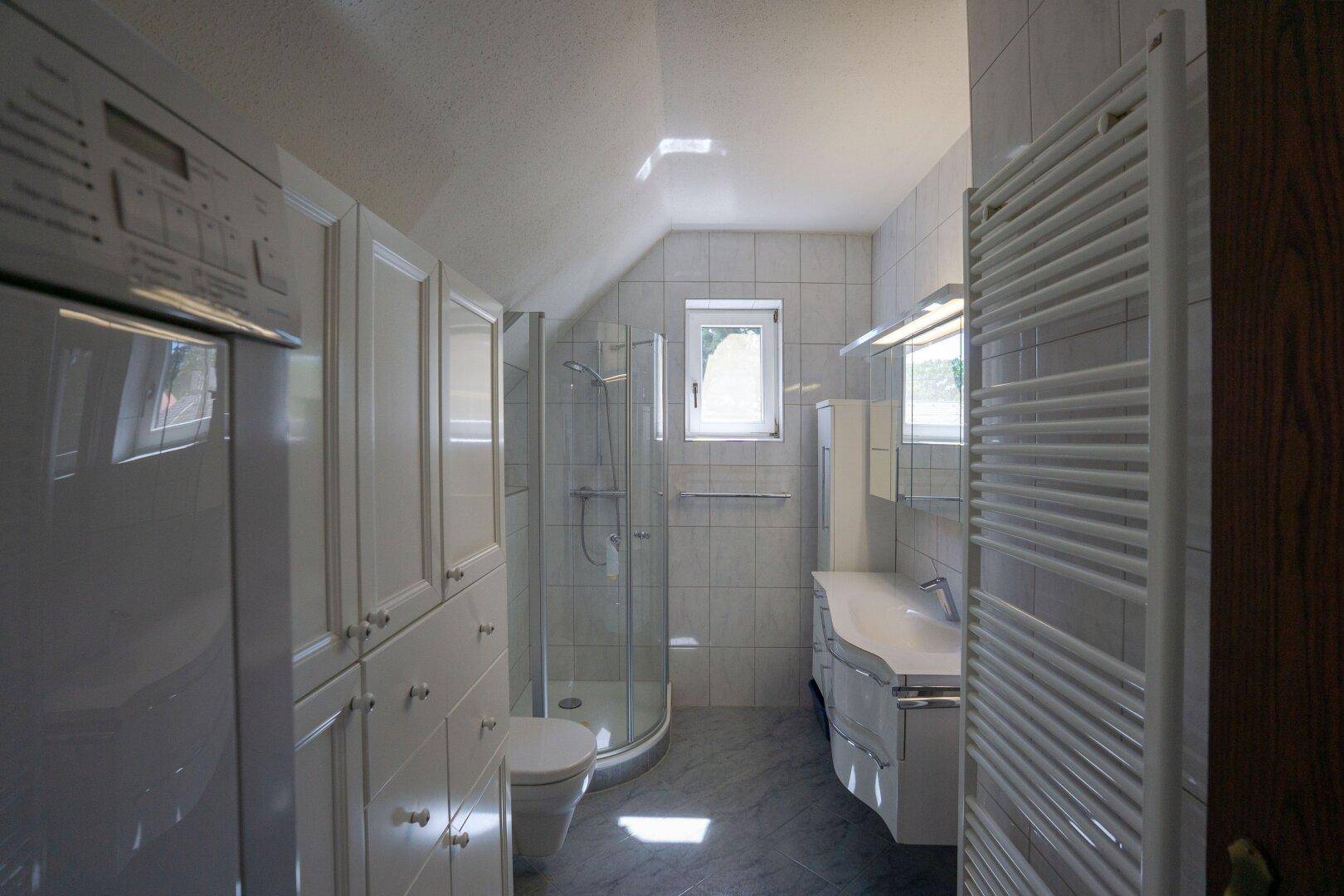 Modernes Badezimmer mit Dusche, weißen Schränken und Dachfenster für natürliches Licht.