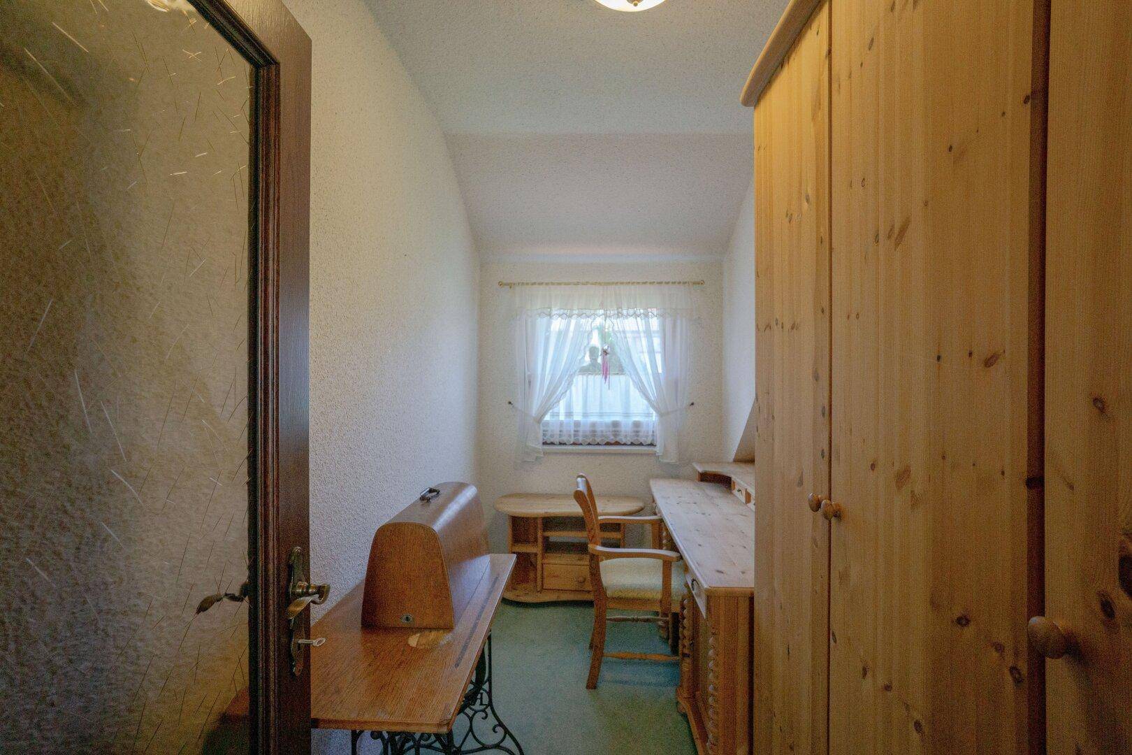 Kleines Arbeitszimmer mit Holzmöbeln und einem Fenster, das Tageslicht hereinlässt.