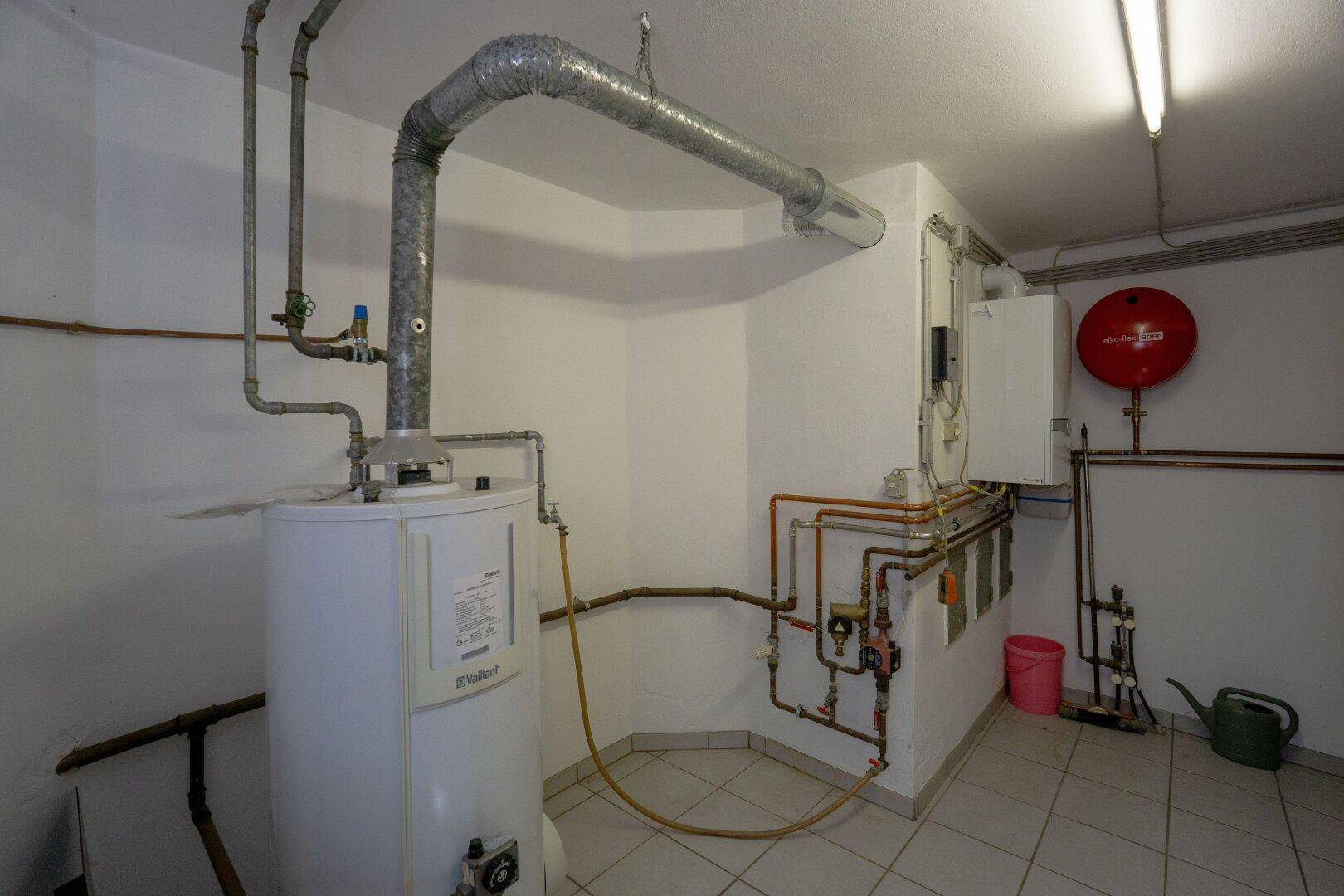Heizraum mit Warmwasserspeicher und sichtbaren Rohrleitungen, sauber und funktional gefliest.
