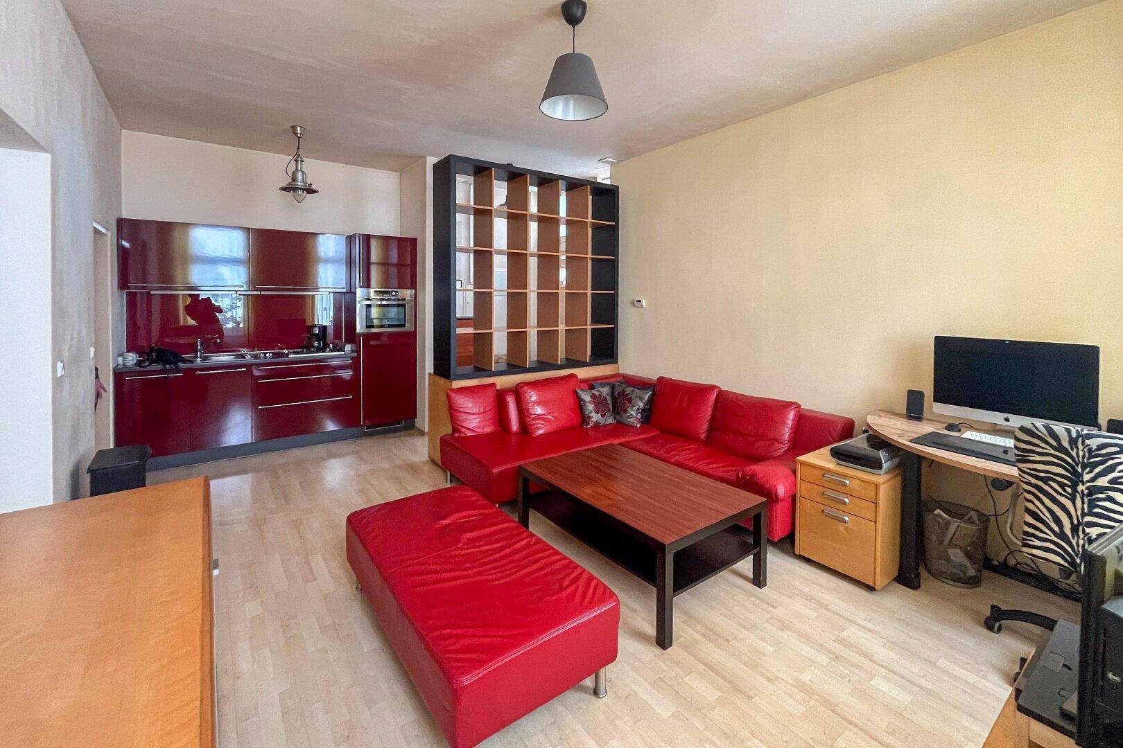 Offener Wohnbereich mit roter Ledercouch, Holzboden und integrierter roter Küche.